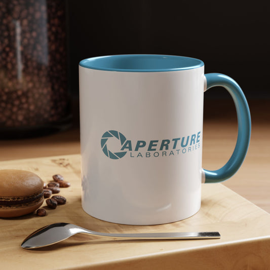 White mug with blue interior and handle featuring 'Aperture Laboratories' logo, placed on a wooden surface with coffee beans and a spoon.