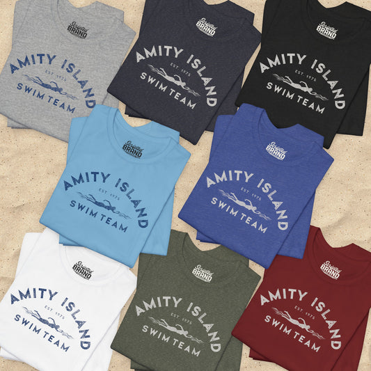 Eight folded tees on a beach with vintage distressed Amity Island Swim Team Jaws-inspired swimmer logo