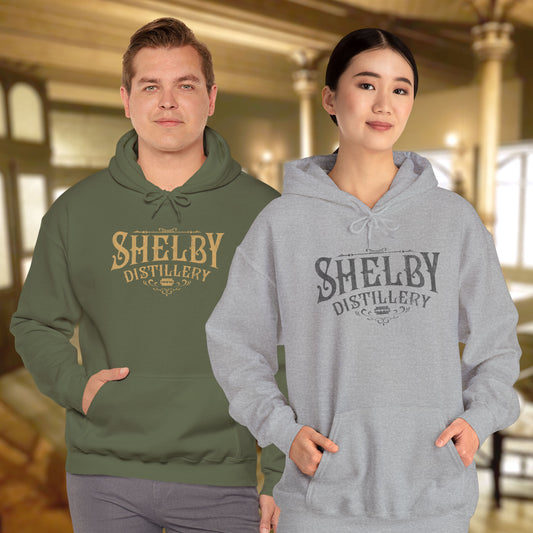 2 models wearing military green and heather gray Unisex Hoodie Heavy Blend Hooded Sweatshirts featuring the Shelby Company Limited Distillery Logo Graphic inspired by the TV show and movie Peaky Blinders in a vintage distressed ink-stamped worn-in style.