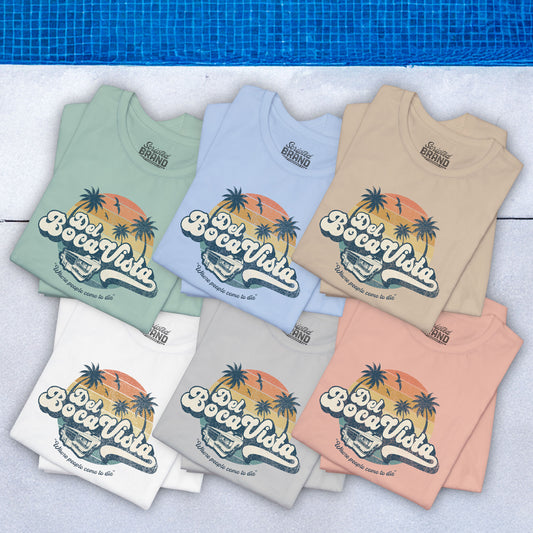 Six folded Bella+Canvas 3001 t-shirts featuring a Del Boca Vista graphic with the phrase Where People Come To Die, inspired by Seinfeld, in a vintage distressed style, laid out near a pool.