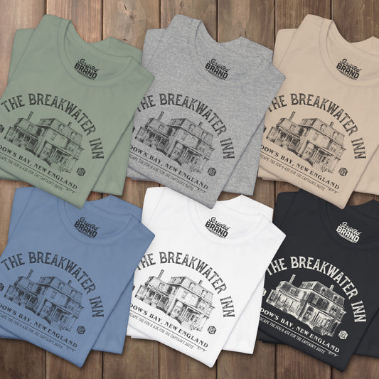 Six folded 'The Breakwater Inn' vintage illustrated t-shirts inspired by Widow's Bay Apple TV series, soft Bella+Canvas cotton fan tee