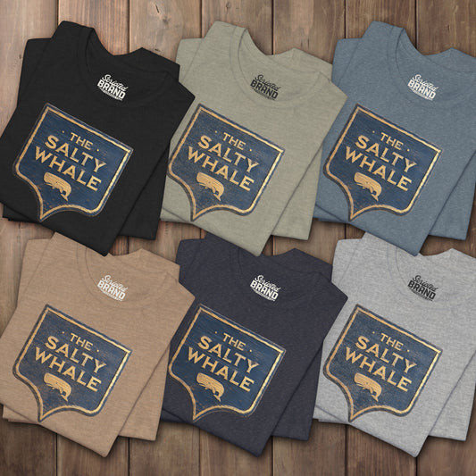 Six folded 'The Salty Whale' weathered carved-wood pub sign t-shirts inspired by Widow's Bay Apple TV series, heather Bella+Canvas tee