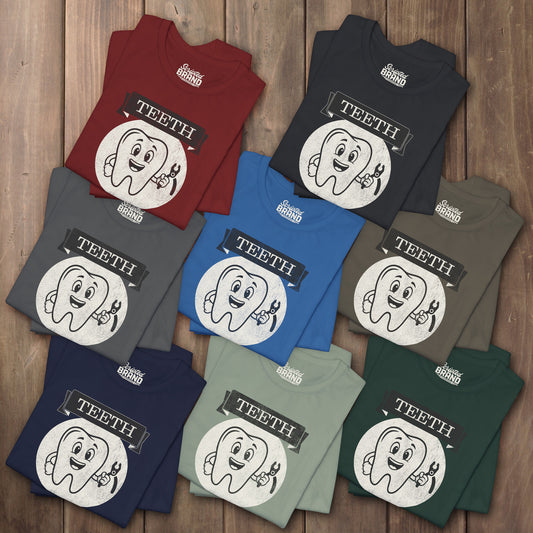 Eight folded Bella+Canvas tees with the vintage TEETH board game box cover from Widow's Bay, a smiling tooth holding pliers