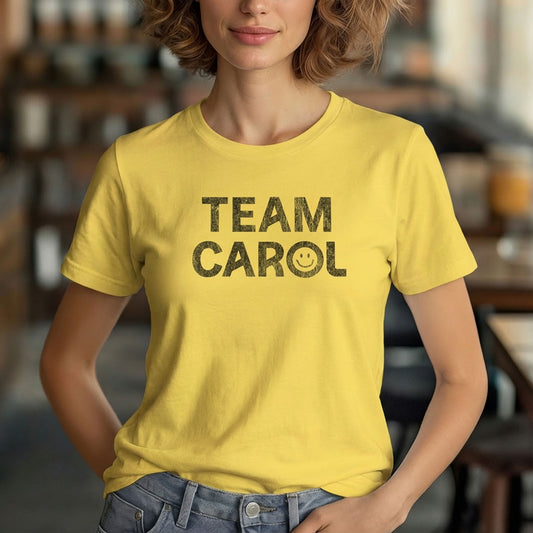 Woman wearing yellow TEAM CAROL t-shirt inspired by Pluribus, smiley face vintage distressed graphic in black