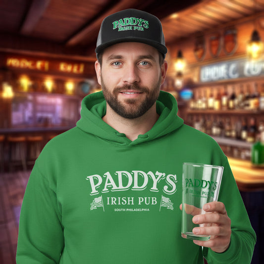 Man wearing a green 'Paddy's Irish Pub' hoodie and hat, and also holding a pint glass in a bar setting.