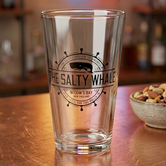 Clear 16 oz pint glass with the vintage black Salty Whale maritime crest logo from Widow's Bay, shown bar with nuts
