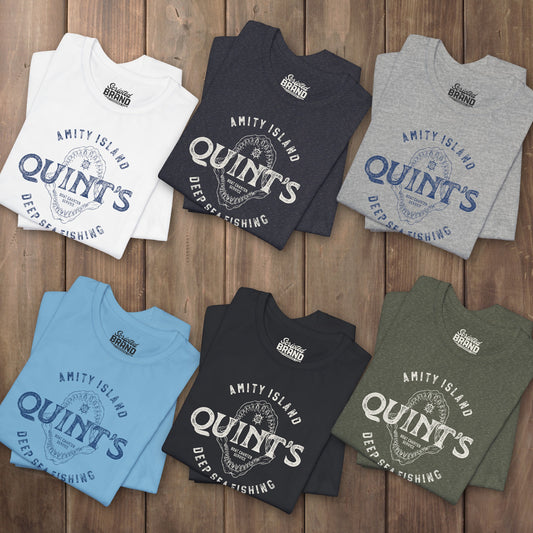 Six folded t-shirts featuring the Quint's Deep Sea Fishing Boat Charters logo graphic inspired by the movie Jaws in a vintage distressed style.