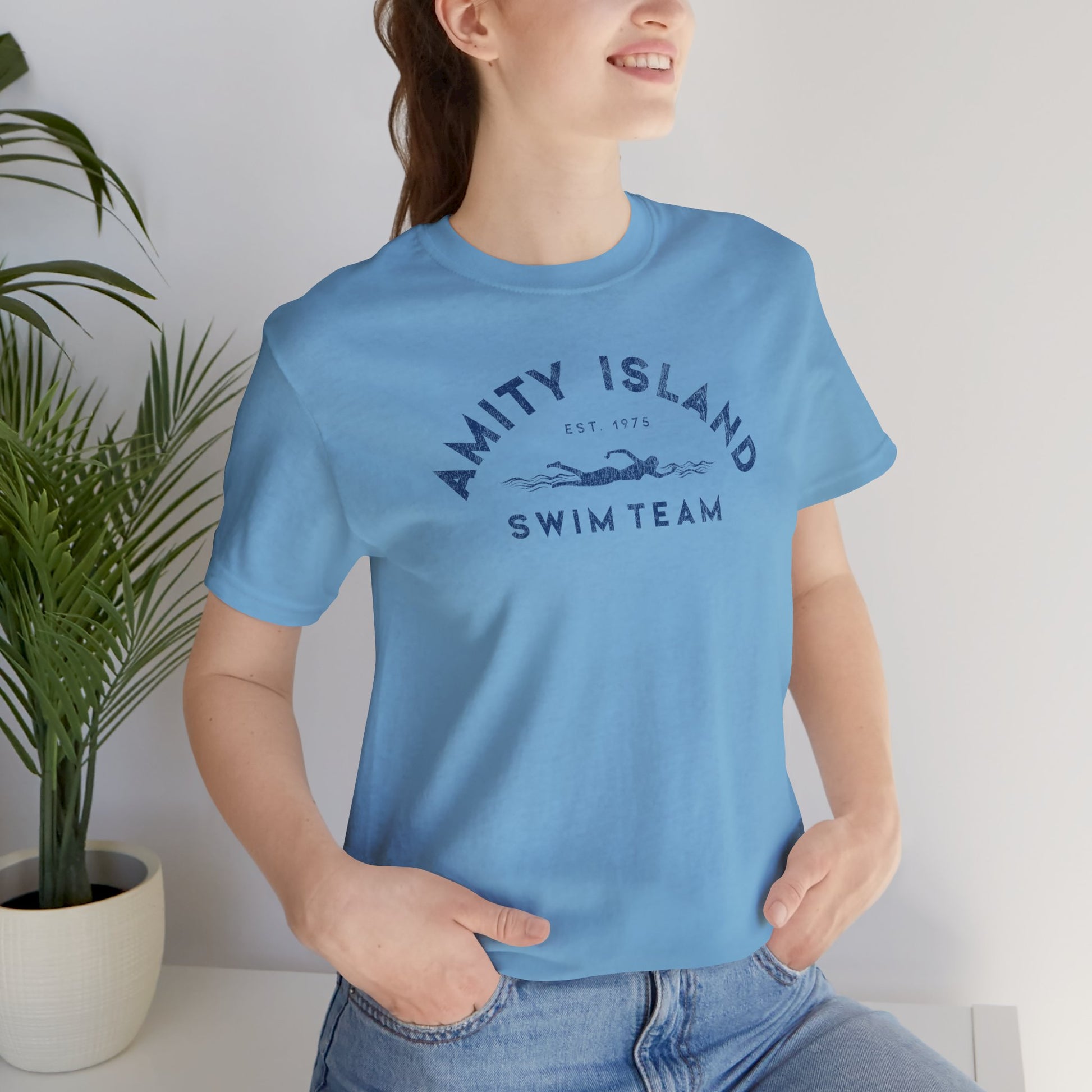 Woman wearing Ocean light Blue tee with vintage distressed Amity Island Swim Team Jaws-inspired swimmer logo