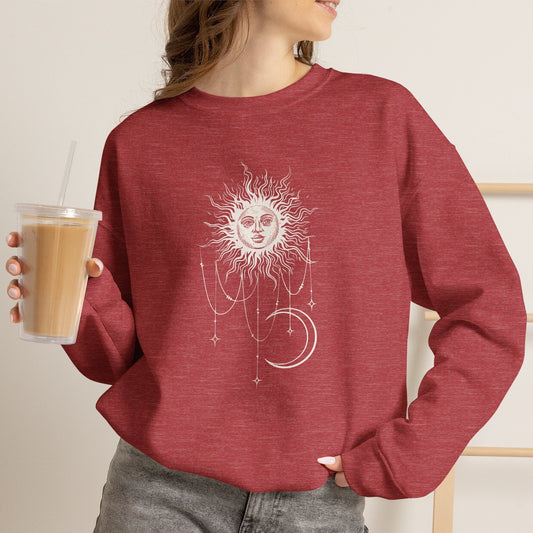 Person wearing Heather red crewneck sweatshirt with boho celestial sun face, stars, and crescent moon design worn by Patricia in Widow's Bay
