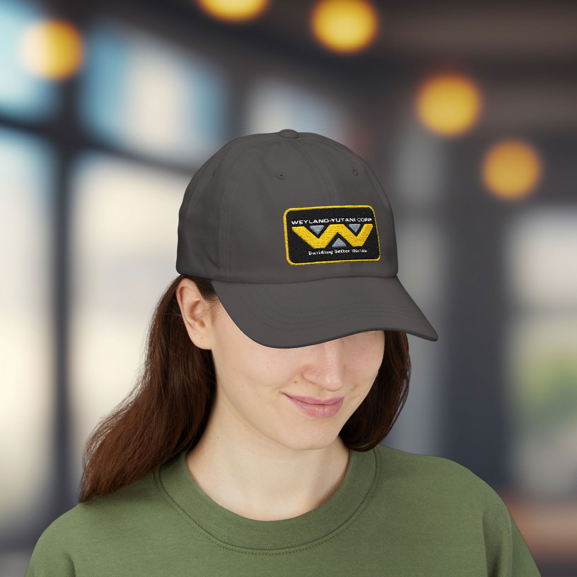 Woman wearing dark grey Yupoong dad cap with embroidered Weyland-Yutani Corp patch logo from the Alien franchise in yellow and silver