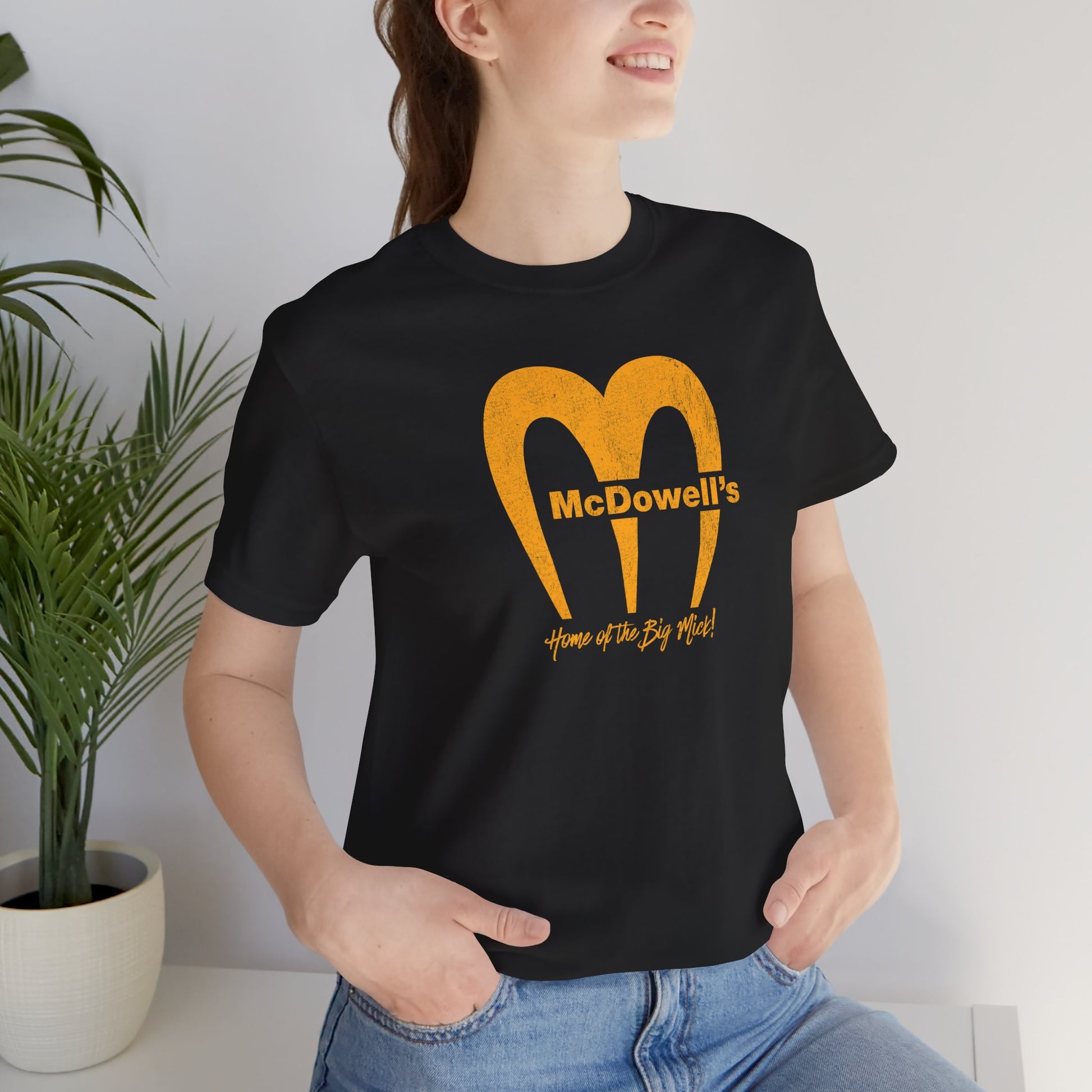 Person wearing Bella+Canvas t-shirt featuring the McDowells logo from the movie Coming to America in a vintage distressed style.