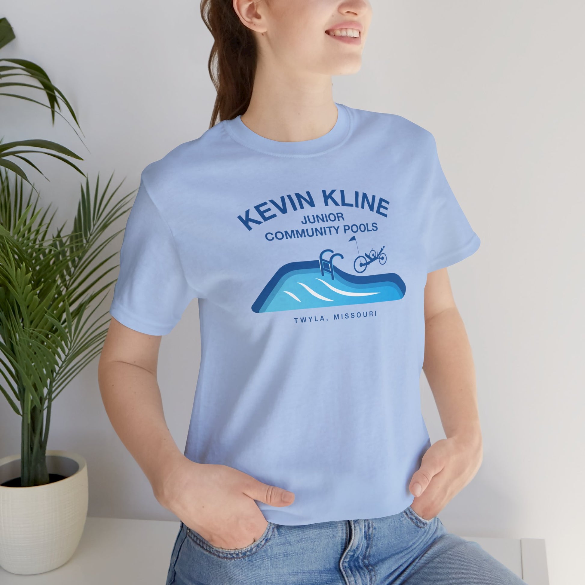 Woman wearing light blue DTF St. Louis Kevin Kline Junior Community Pools graphic tee with pool and recumbent trike.