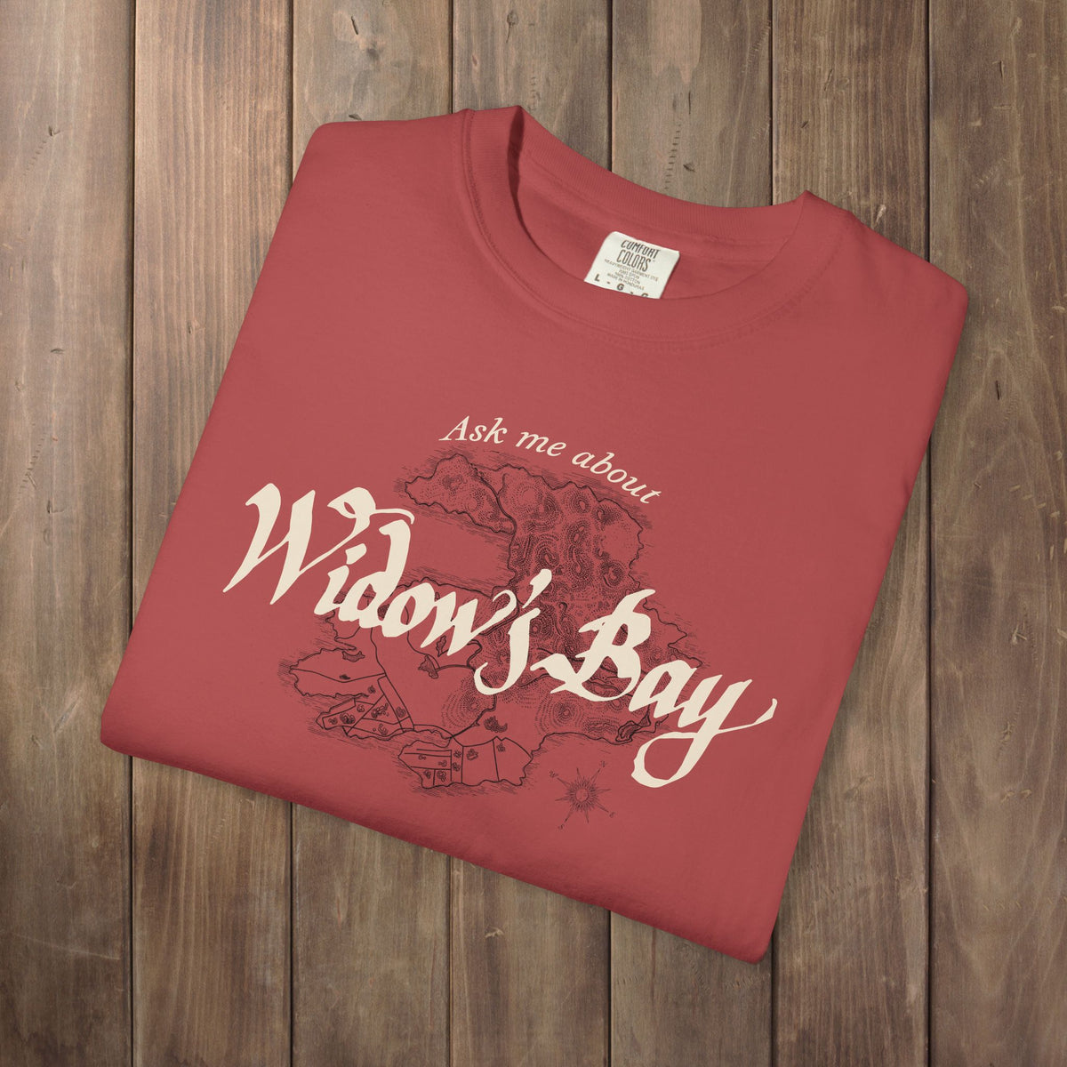 Folded Crimson Comfort Colors tee with a vintage island map and antique "Ask Me About Widow's Bay" type from the Apple TV show