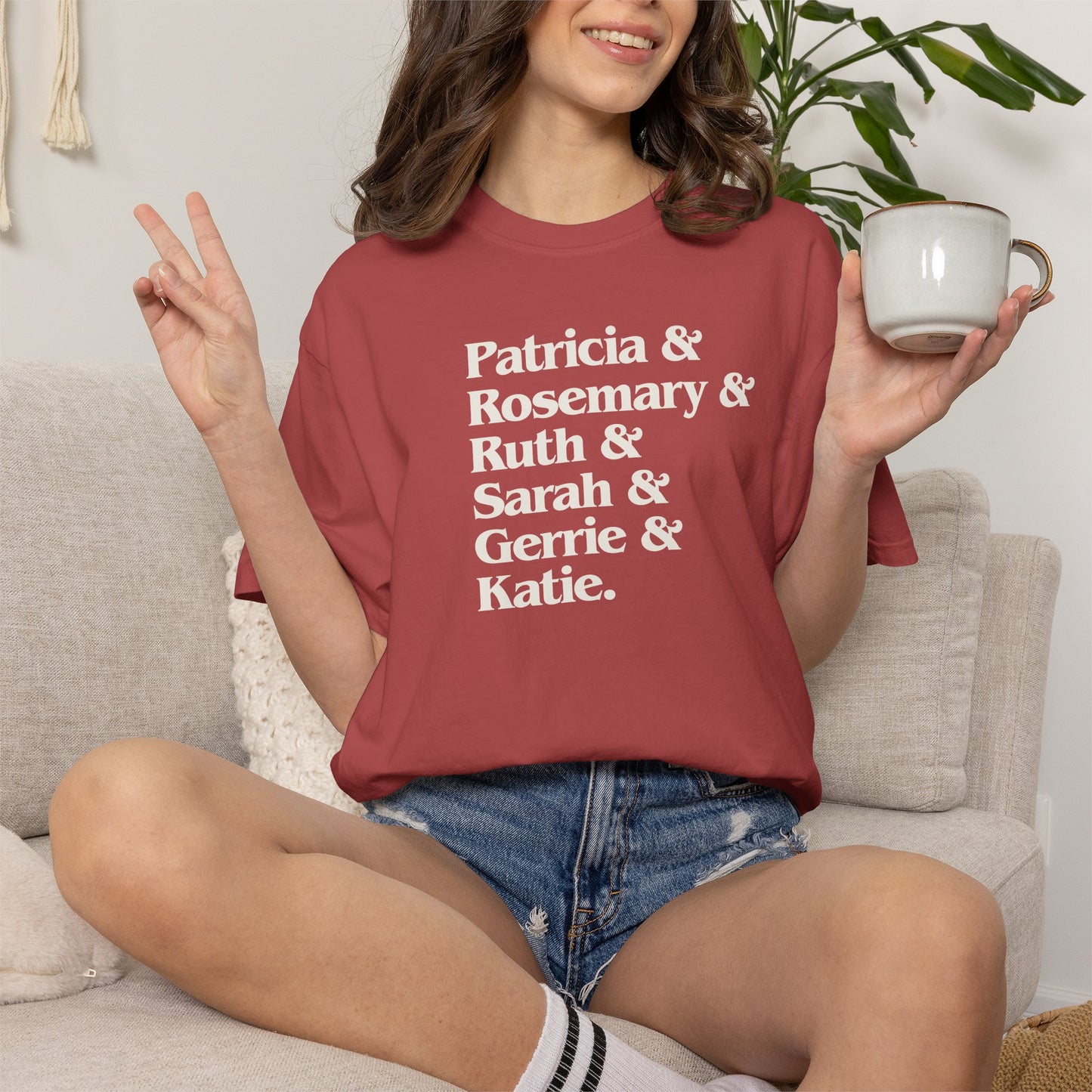Woman sitting wearing Crimson Comfort Colors tee listing the women of Widow's Bay: Patricia, Rosemary, Ruth, Sarah, Gerrie, and Katie