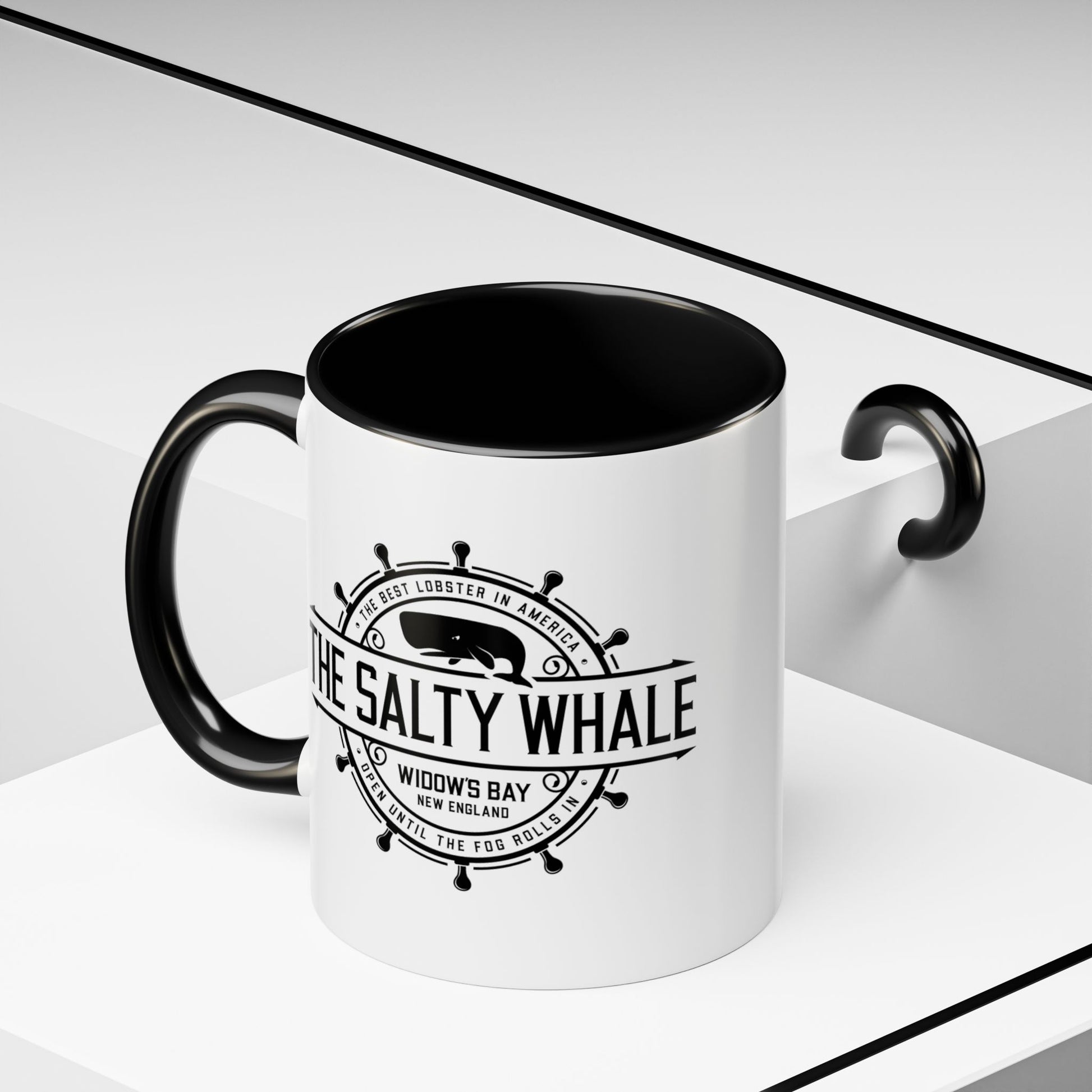 Angled view of 11 oz White ceramic mug with black handle and the vintage Salty Whale maritime crest logo from Widow's Bay TV show, New England