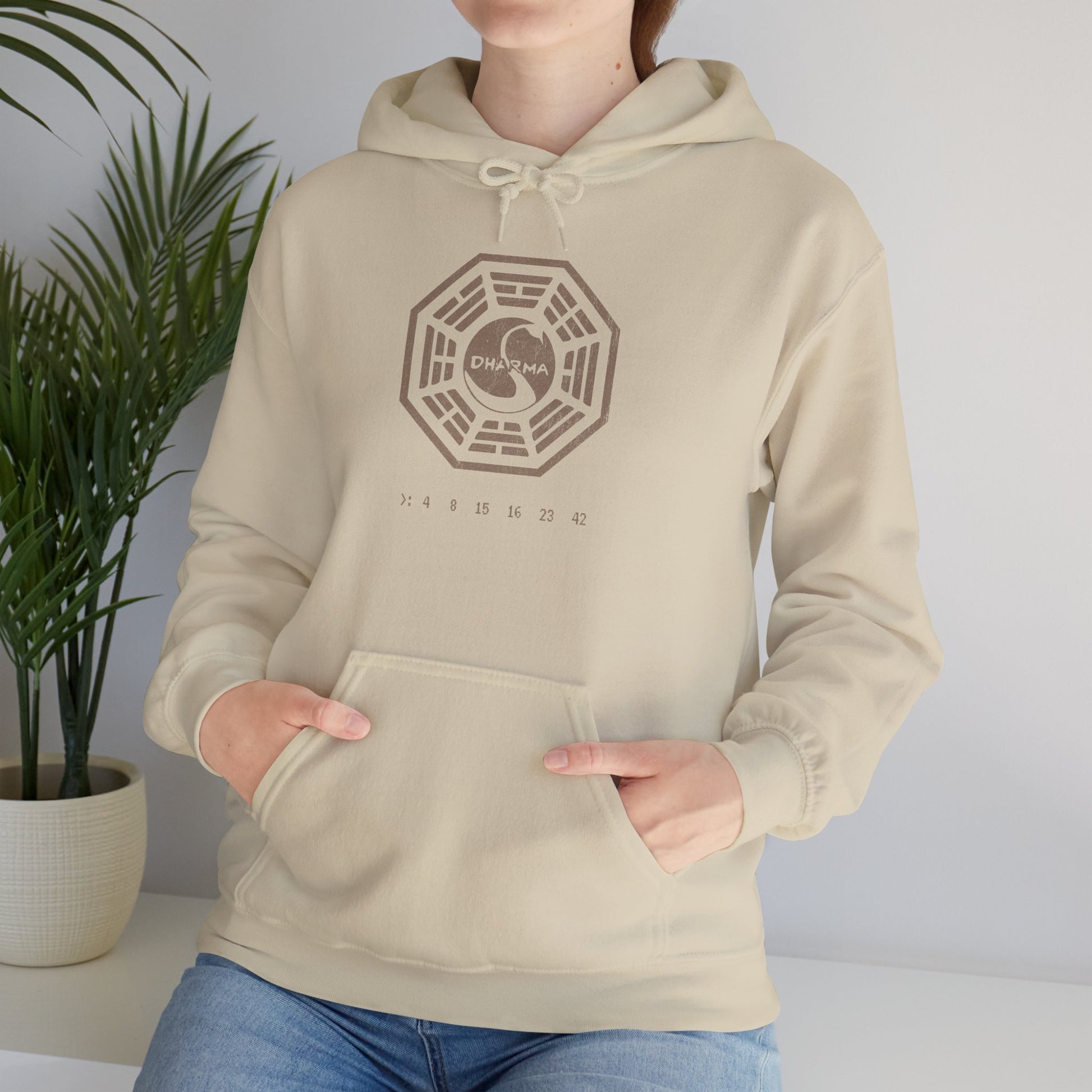 Female model wearing a sand Unisex Hoodie Heavy Blend Hooded Sweatshirt featuring the Dharma Initiative swan logo graphic from the TV show LOST in a vintage distressed ink-stamped worn-in style.