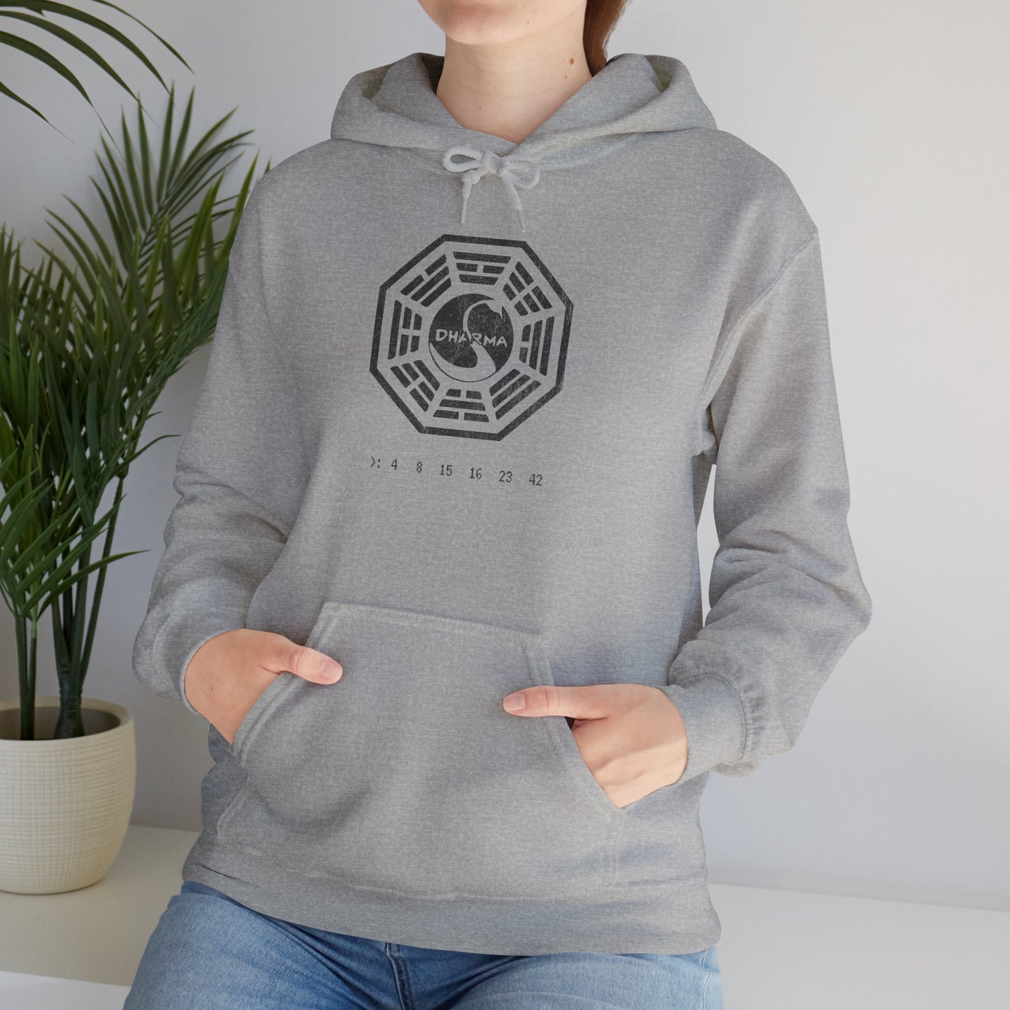Female model wearing a sport heather gray Unisex Hoodie Heavy Blend Hooded Sweatshirt featuring the Dharma Initiative swan logo graphic from the TV show LOST in a vintage distressed ink-stamped worn-in style.
