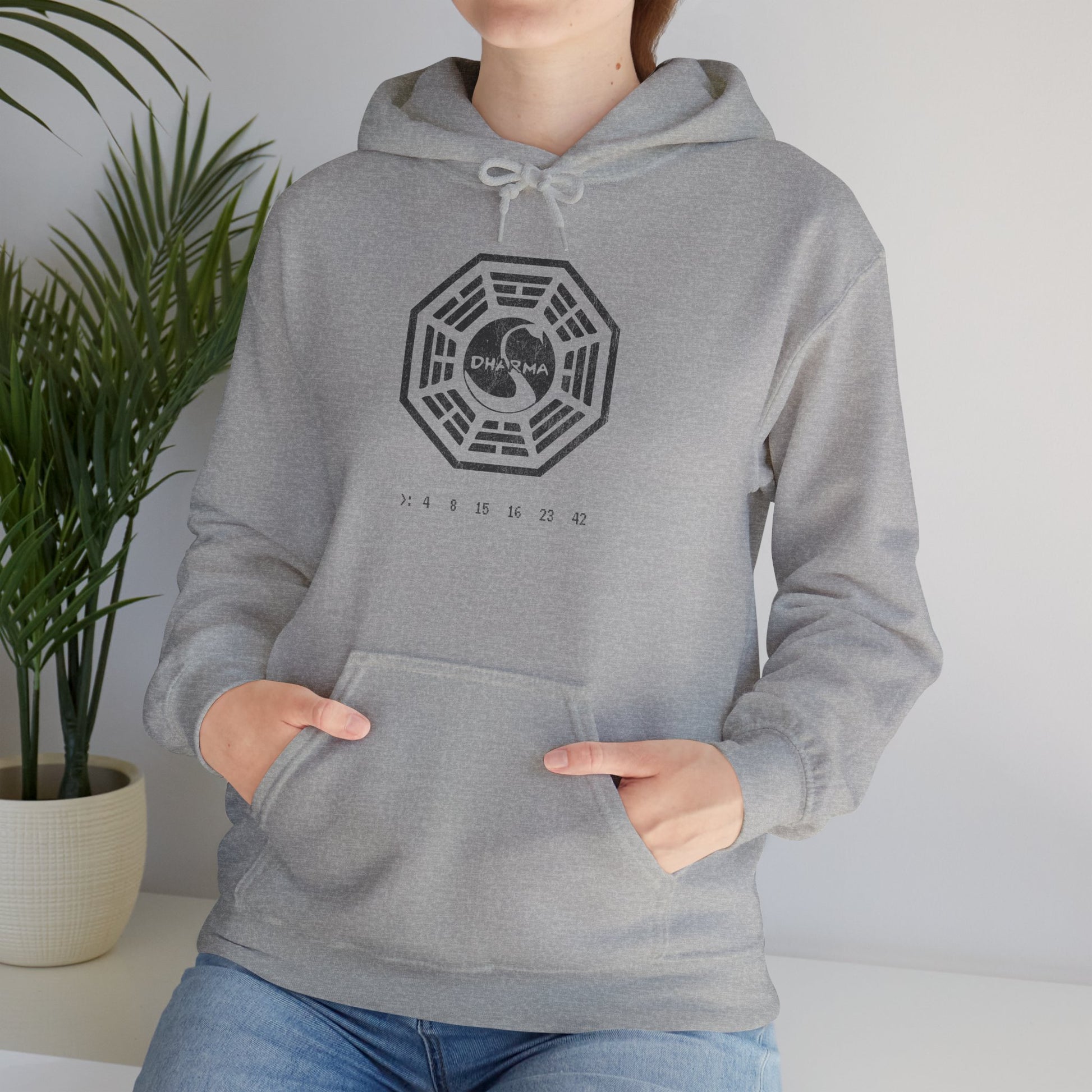 Female model wearing a sport heather gray Unisex Hoodie Heavy Blend Hooded Sweatshirt featuring the Dharma Initiative swan logo graphic from the TV show LOST in a vintage distressed ink-stamped worn-in style.