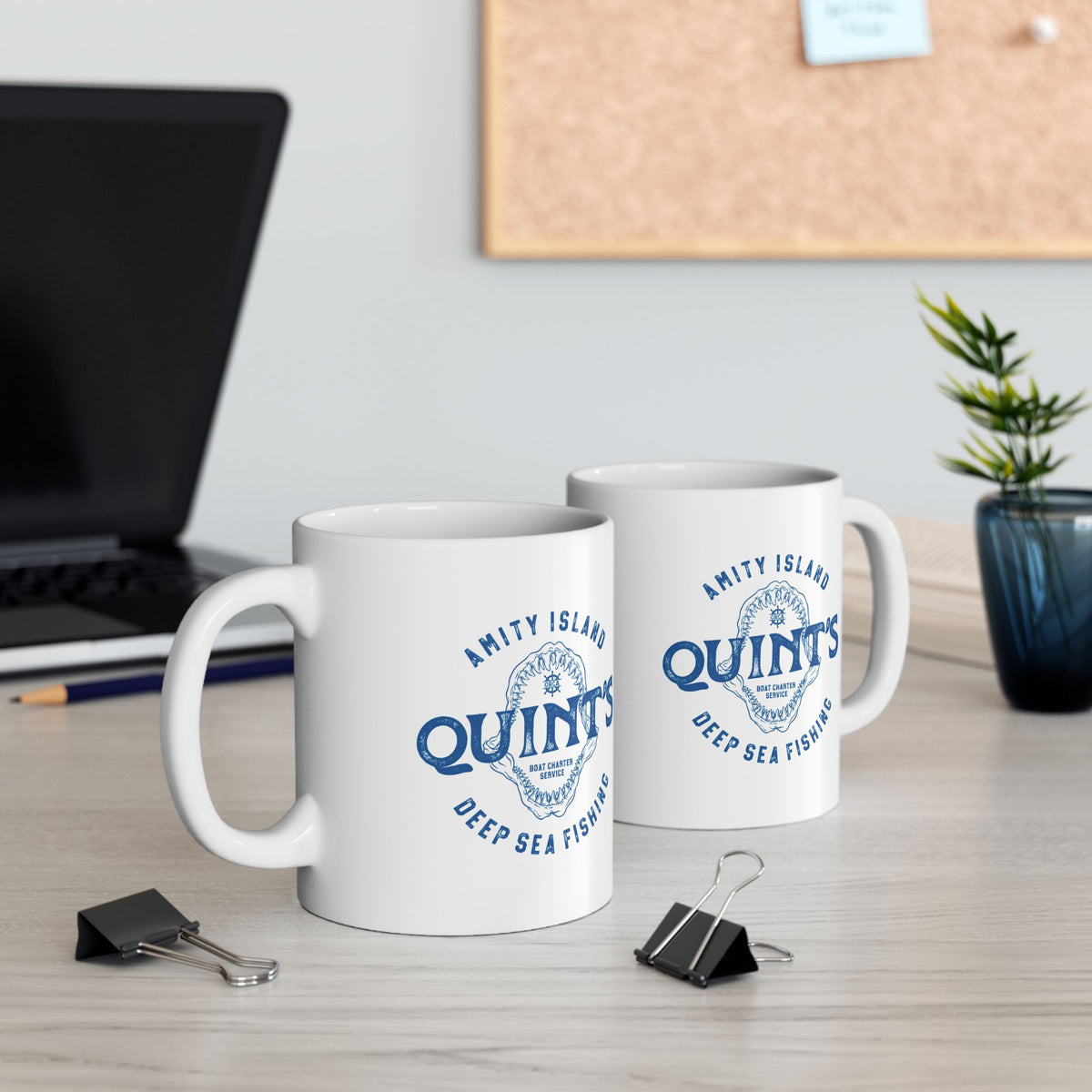 2 White mugs with blue Amity Island Quint's Deep Sea Fishing boat charter logo and shark jaws, inspired by Jaws, on a desk