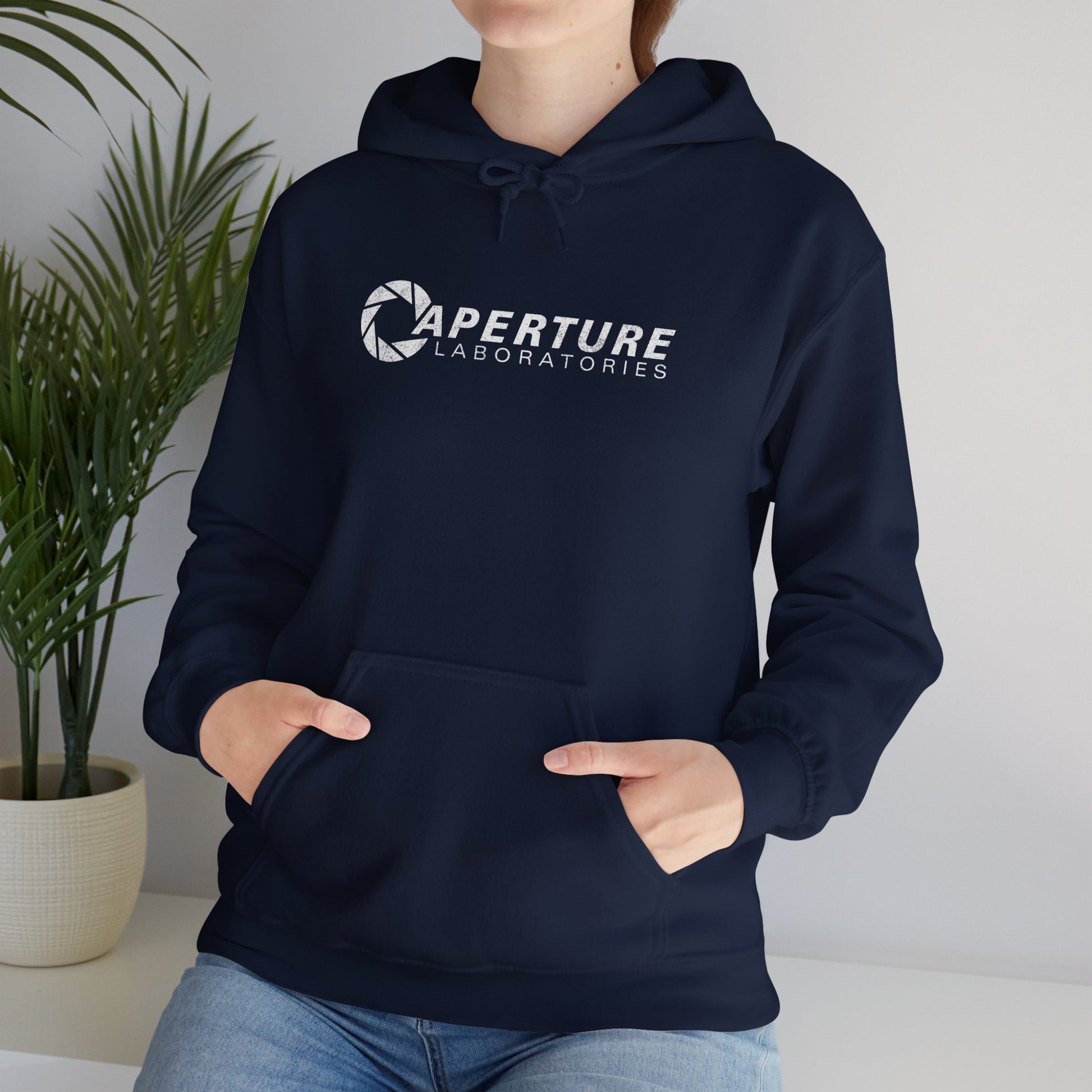 Female model wearing a navy blue colored Unisex Hoodie Heavy Blend Hooded Sweatshirt featuring the Aperture Laboratories logo from the video game Portal and Portal 2 in a vintage distressed style, sold by ScriptedBrand.