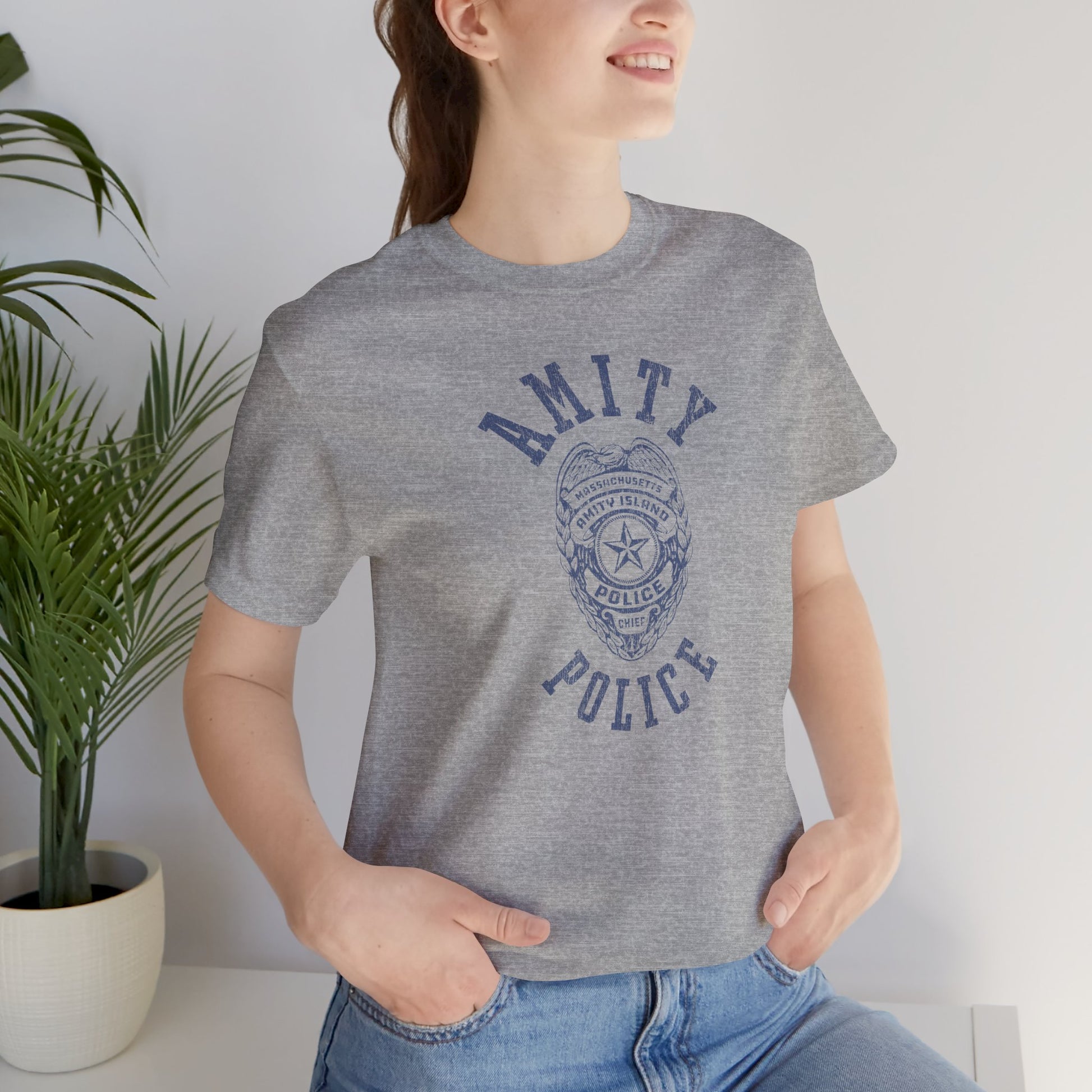 Female model wearing an athletic heather grey colored Soft unisex Bella+Canvas 3001 short-sleeve t-shirt featuring an Amity Island Police logo graphic, designed by ScriptedBrand, and  inspired by the movie Jaws in a vintage distressed style.