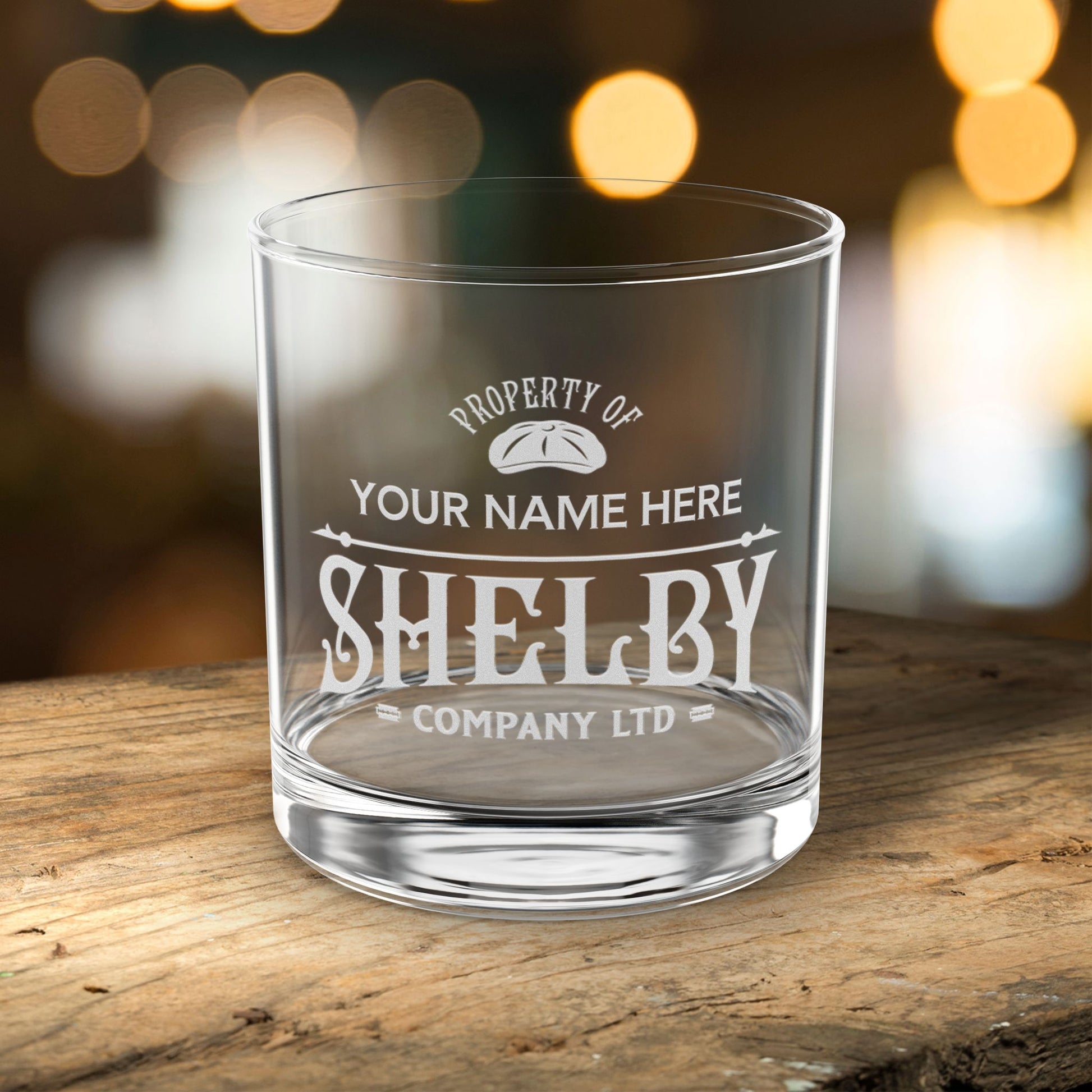 Clear glass tumbler with engraved text on a wooden surface with blurred lights in the background