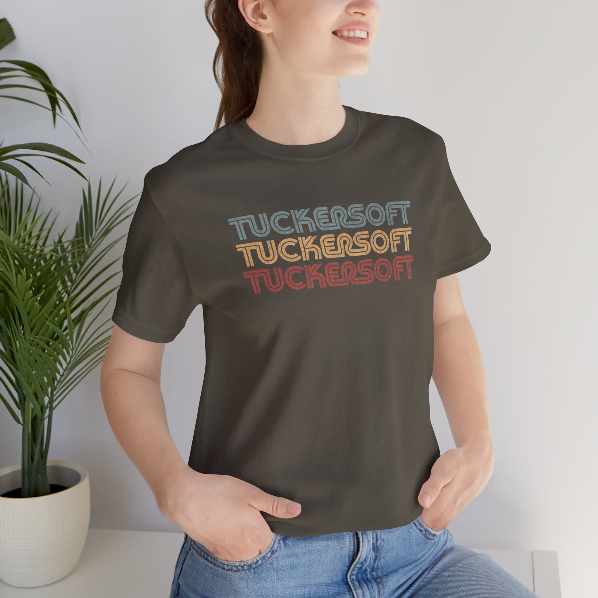 Female model wearing an army colored soft Bella+Canvas 3001 short-sleeve t-shirt tee featuring a logo graphic of the 1980s fictional video game company Tuckersoft inspired by the TV show Black Mirror and the episode Bandersnatch in a vintage distressed style, sold by ScriptedBrand.