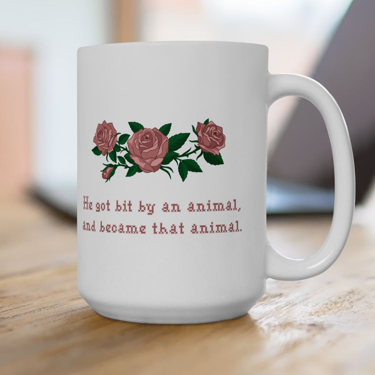 15oz white ceramic mug with a printed design of pink roses and green leaves, featuring the text 'He got bit by an animal, and became that animal' in cross stitch style, inspired by Ruth on Widows Bay