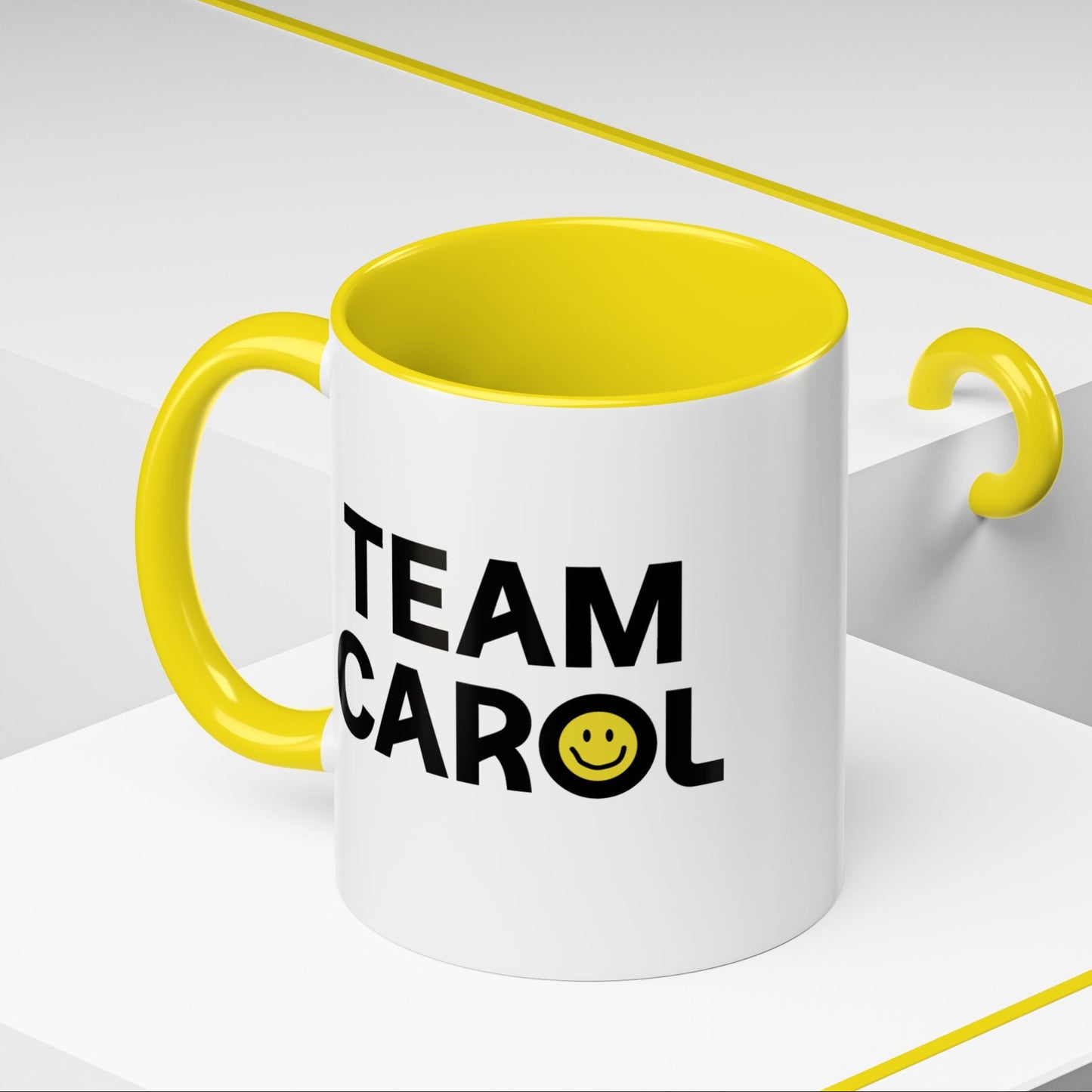 Angled view of 11 oz ceramic accent mug with yellow handle and interior, TEAM CAROL text and smiley face from Pluribus