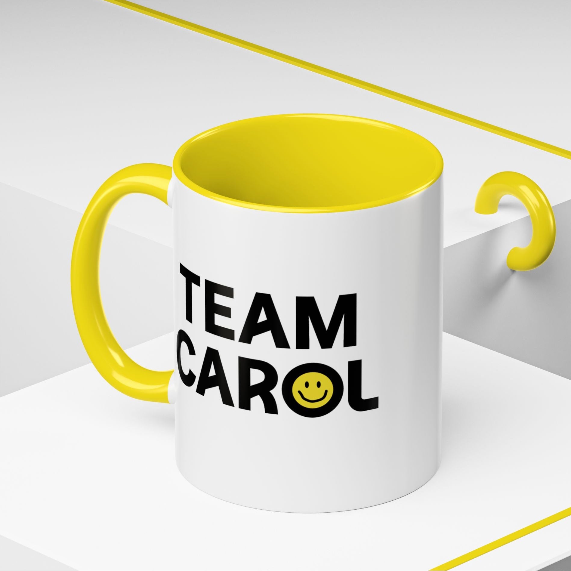 Angled view of 11 oz ceramic accent mug with yellow handle and interior, TEAM CAROL text and smiley face from Pluribus