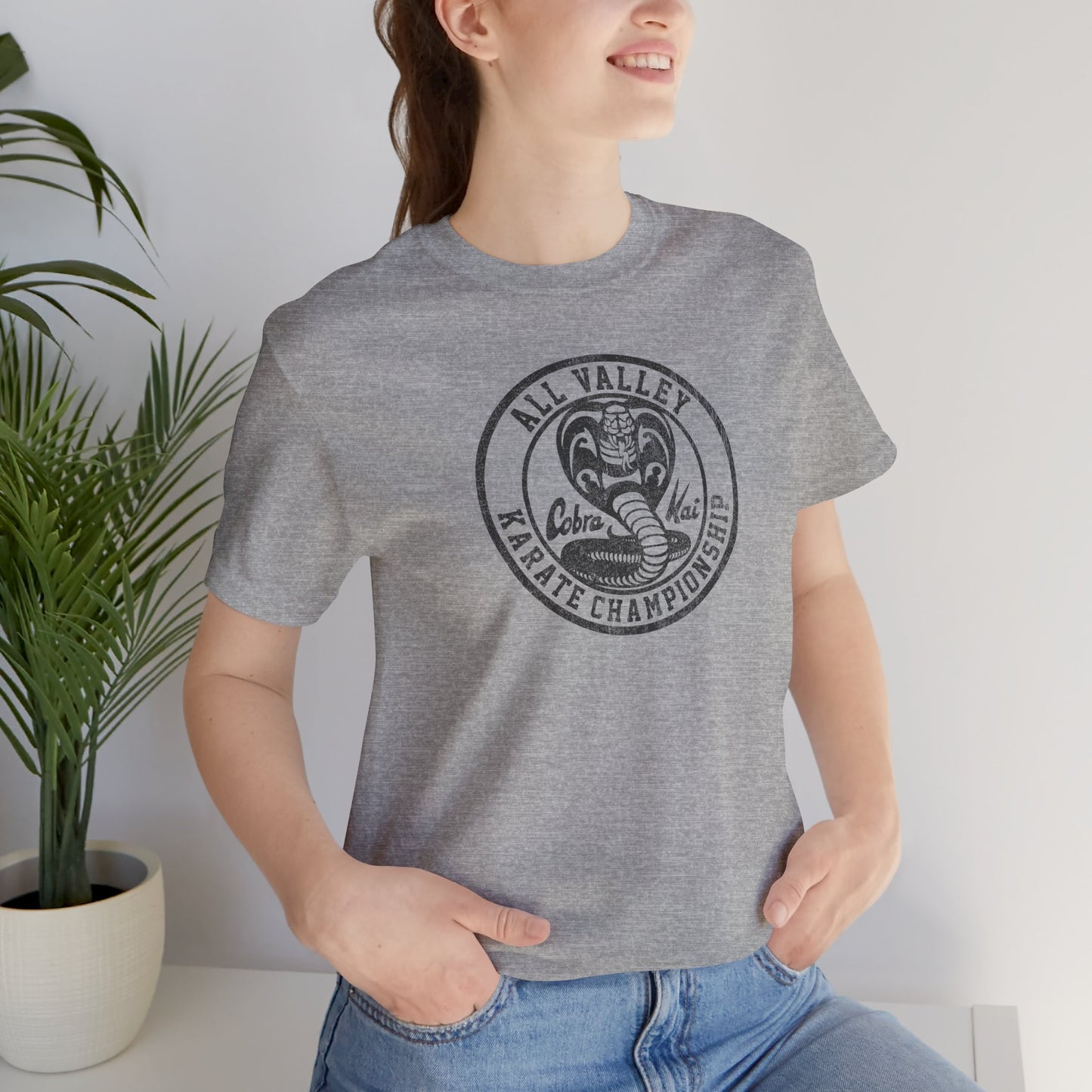 Woman wearing heather gray Cobra Kai All Valley Karate Championship vintage distressed graphic t-shirt, soft Bella+Canvas cotton Karate Kid tee
