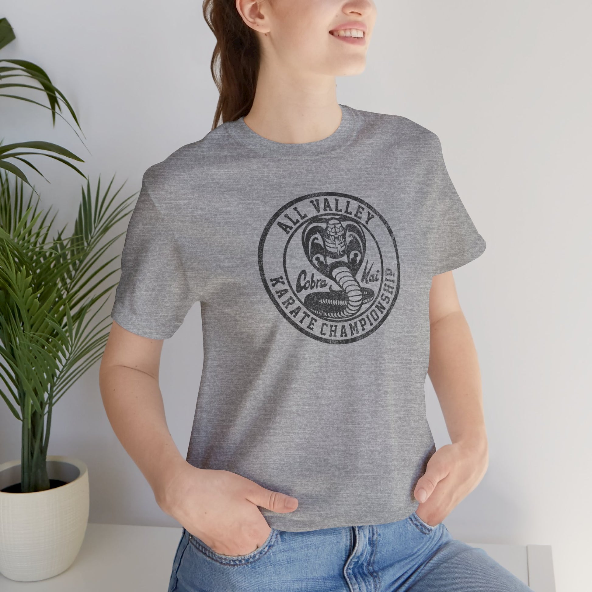 Woman wearing heather gray Cobra Kai All Valley Karate Championship vintage distressed graphic t-shirt, soft Bella+Canvas cotton Karate Kid tee