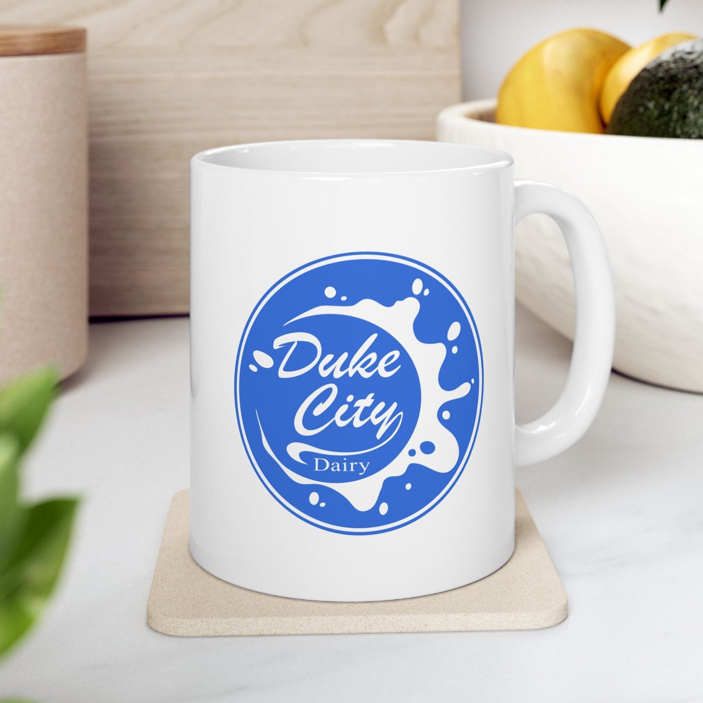 White ceramic mug with the blue Duke City Dairy logo printed on both sides, inspired by the TV show Pluribus, set in a kitchen.