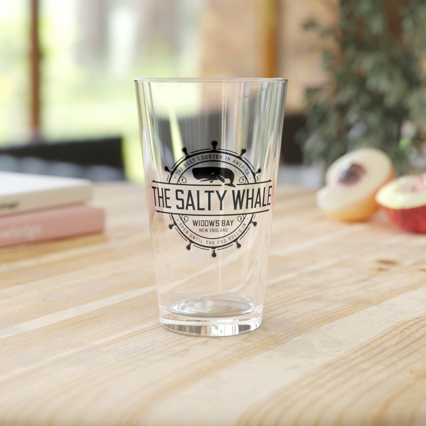 Clear 16 oz pint glass with the vintage black Salty Whale maritime crest logo from Widow's Bay in a kitchen