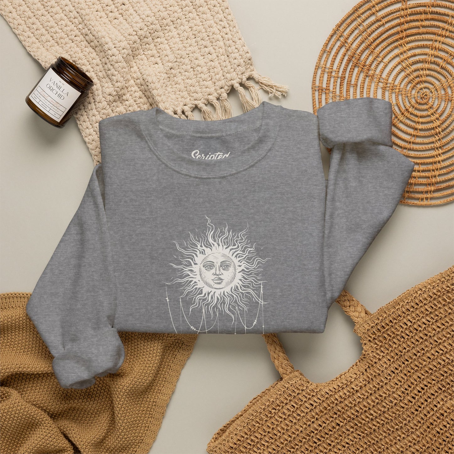 Folded Heather gray crewneck sweatshirt with boho celestial sun face, stars, and crescent moon design worn by Patricia in Widow's Bay
