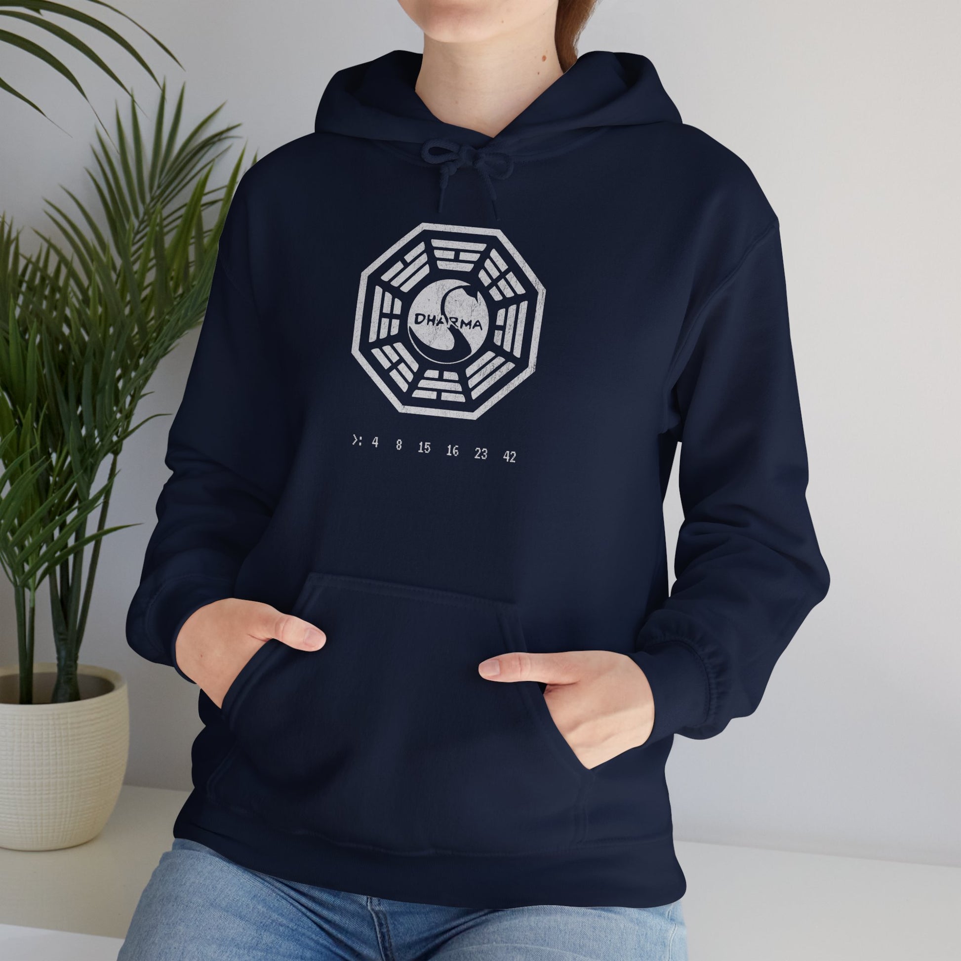 Female model wearing a navy blue Soft Unisex Hoodie Heavy Blend Hooded Sweatshirt featuring the Dharma Initiative swan logo graphic from the TV show LOST in a vintage distressed ink-stamped worn-in style.