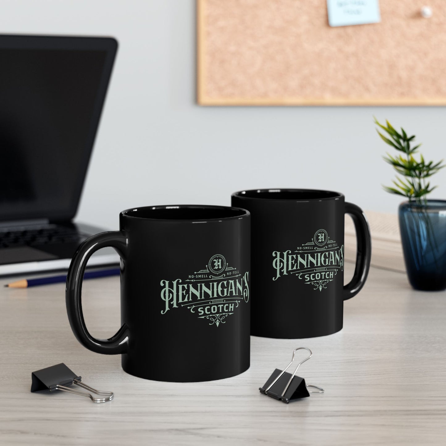 Two black mugs with 'Hennigan's Scotch' branding on a desk with office supplies.