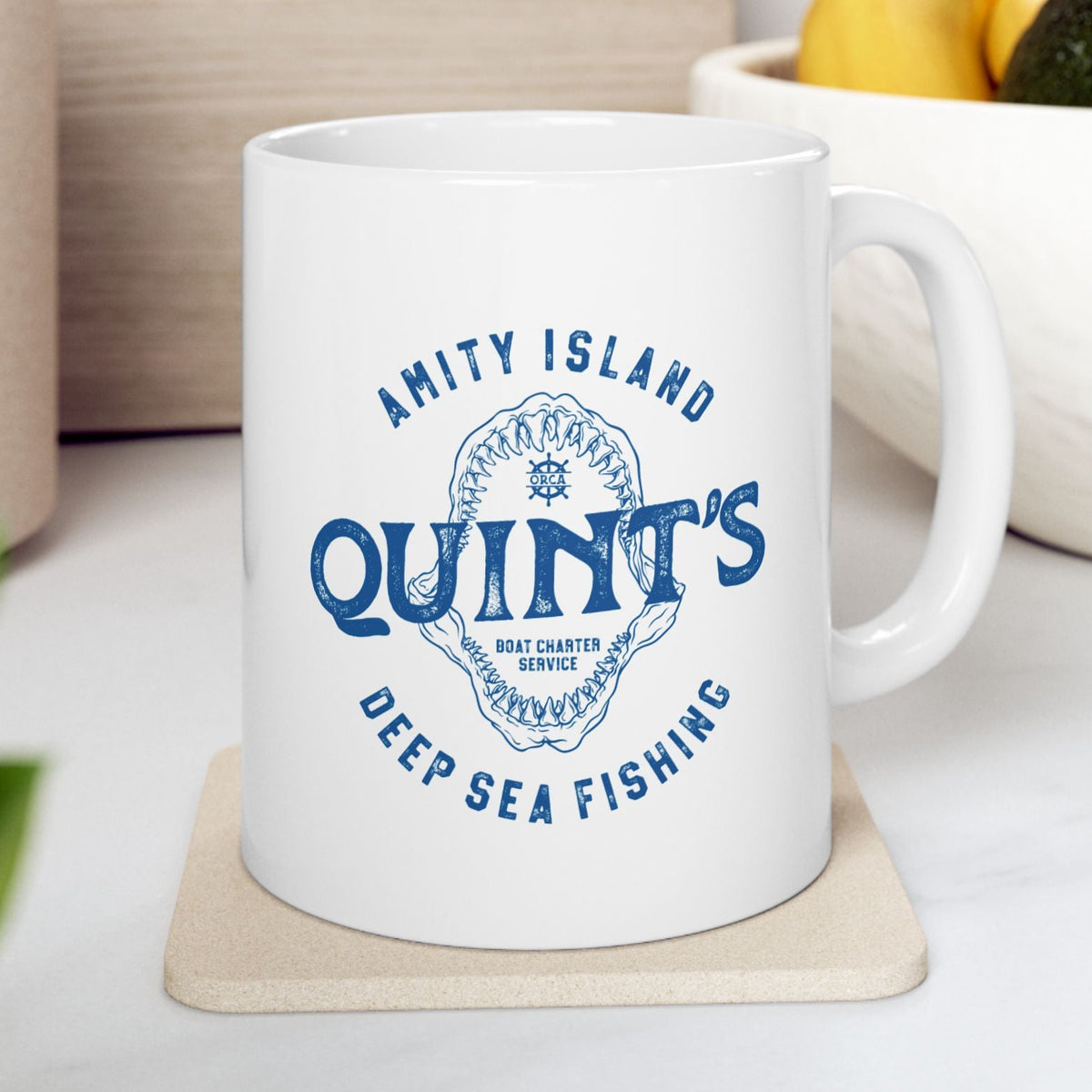 White mug with blue Amity Island Quint's Deep Sea Fishing boat charter logo and shark jaws, inspired by Jaws, in a kitchen