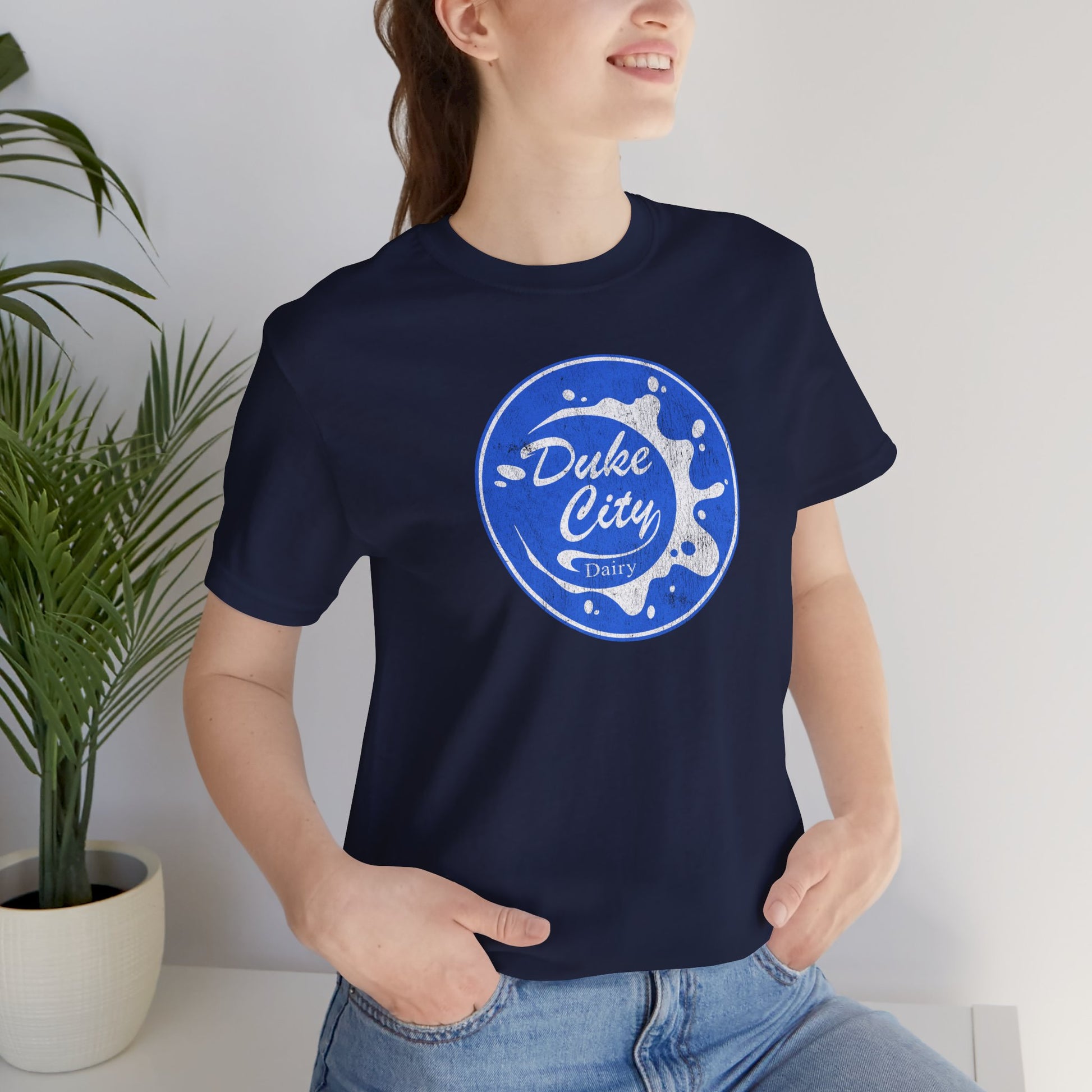 Woman wearing navy blue t-shirt with vintage distressed Duke City Dairy logo inspired by TV Show Pluribus.