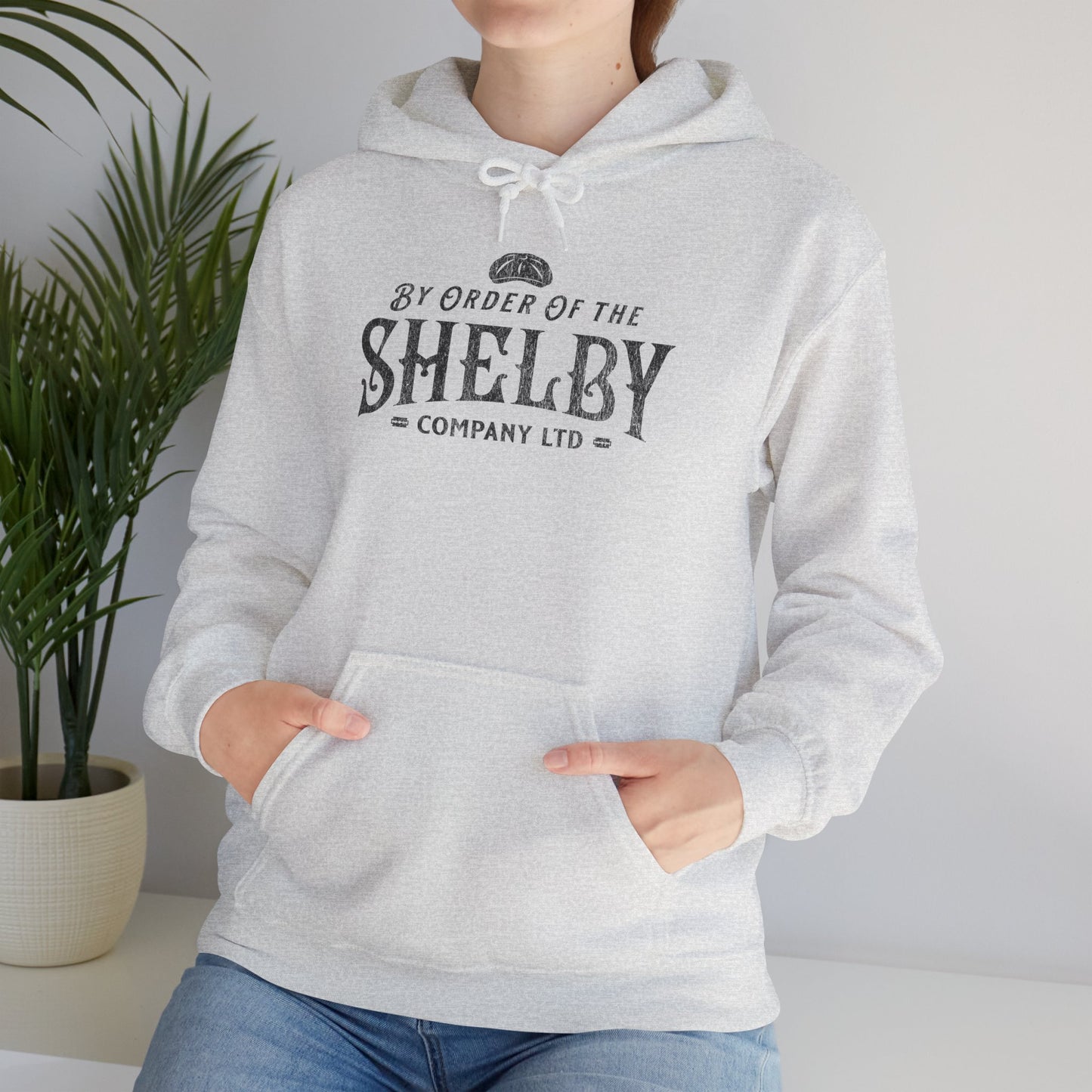 Woman wearing ash Unisex Gildan 18500 Heavy Blend Hoodie Sweatshirt with a vintage Shelby Company Limited logo graphic from Peaky Blinders.