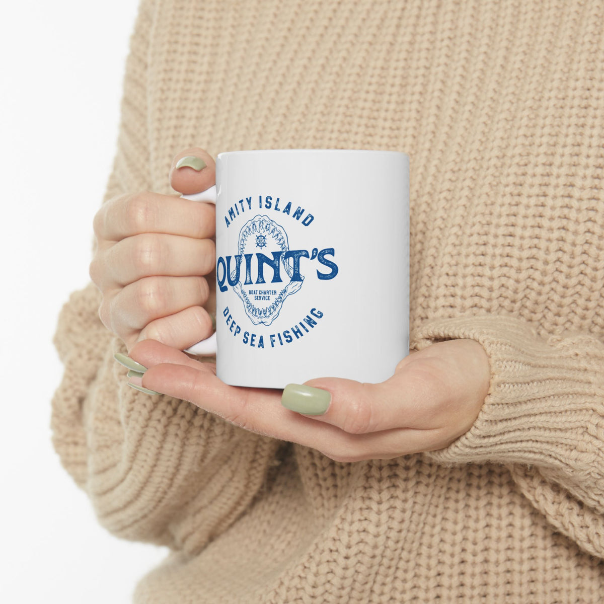 Person holding White mug with blue Amity Island Quint's Deep Sea Fishing boat charter logo and shark jaws, inspired by Jaws, in a cafe