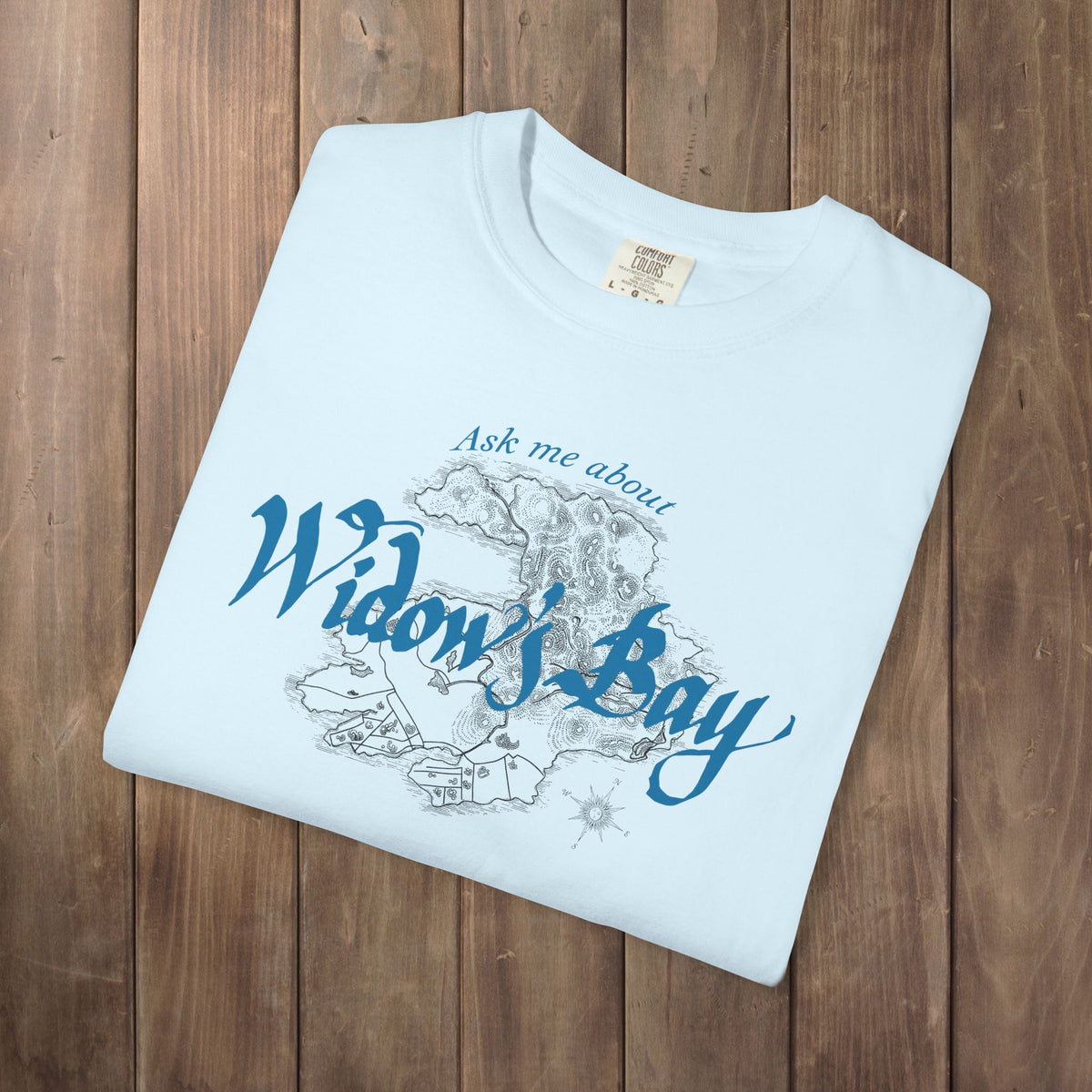 Folded chambray blue Comfort Colors tee with a vintage island map and antique "Ask Me About Widow's Bay" type from the Apple TV show