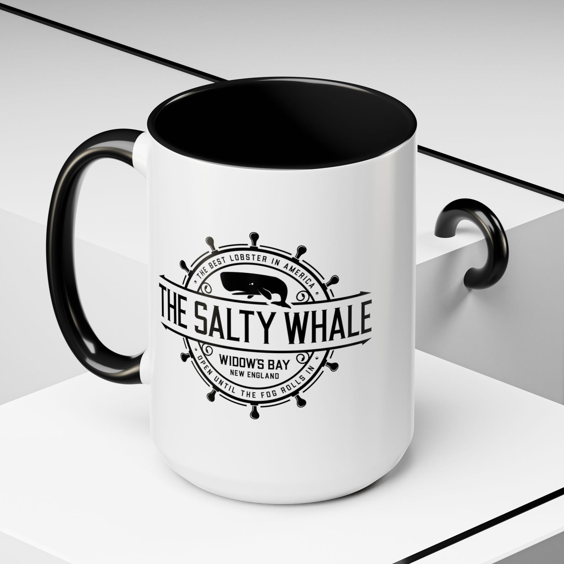 Angled view of 15 oz White ceramic mug with black handle and the vintage Salty Whale maritime crest logo from Widow's Bay TV show, New England