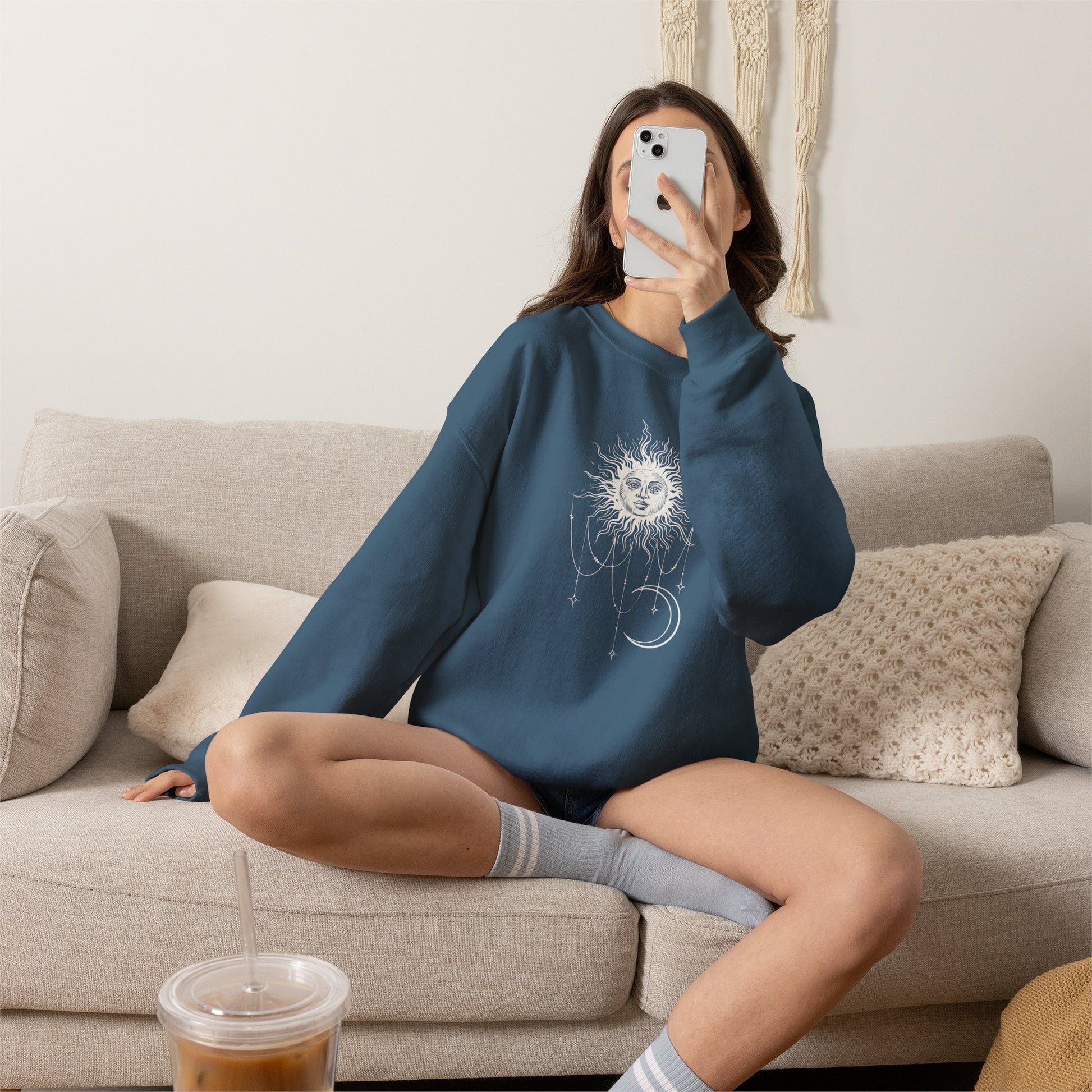 Woman wearing indigo blue crewneck sweatshirt with boho celestial sun face, stars, and crescent moon design worn by Patricia in Widow's Bay