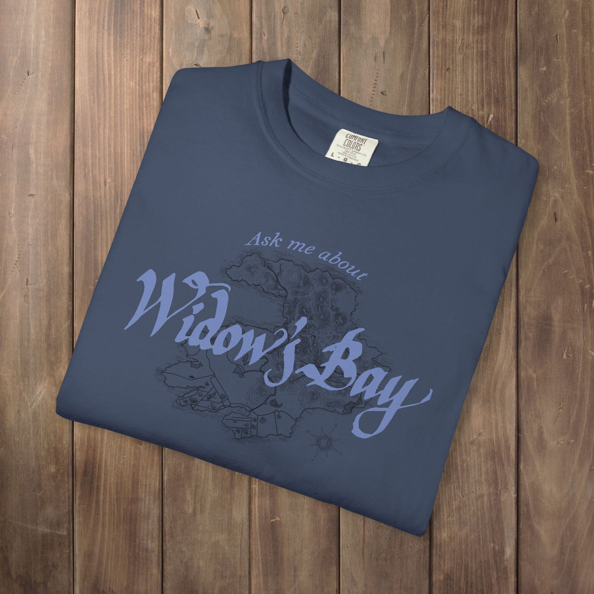 Folded midnight blue Comfort Colors tee with a vintage island map and antique "Ask Me About Widow's Bay" type from the Apple TV show
