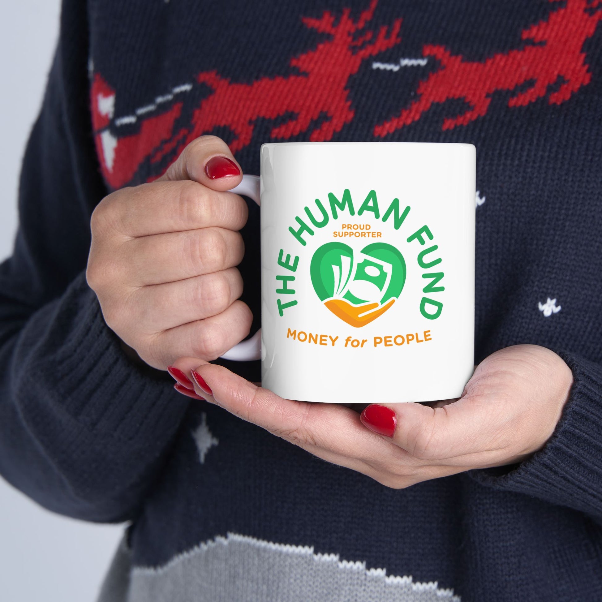 Person holding a mug with 'The Human Fund' logo against a Christmas sweater background