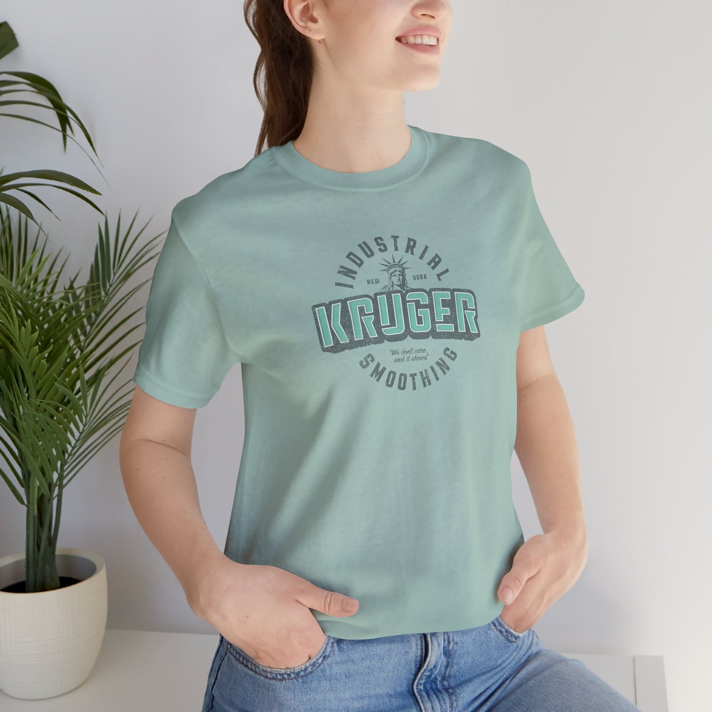 Female model wearing a dusty blue colored Soft unisex Bella+Canvas 3001 short-sleeve t-shirt featuring a Kruger Industrial Smoothing logo graphic in a vintage distressed style, designed by ScriptedBrand, and  inspired by the TV show Seinfeld.