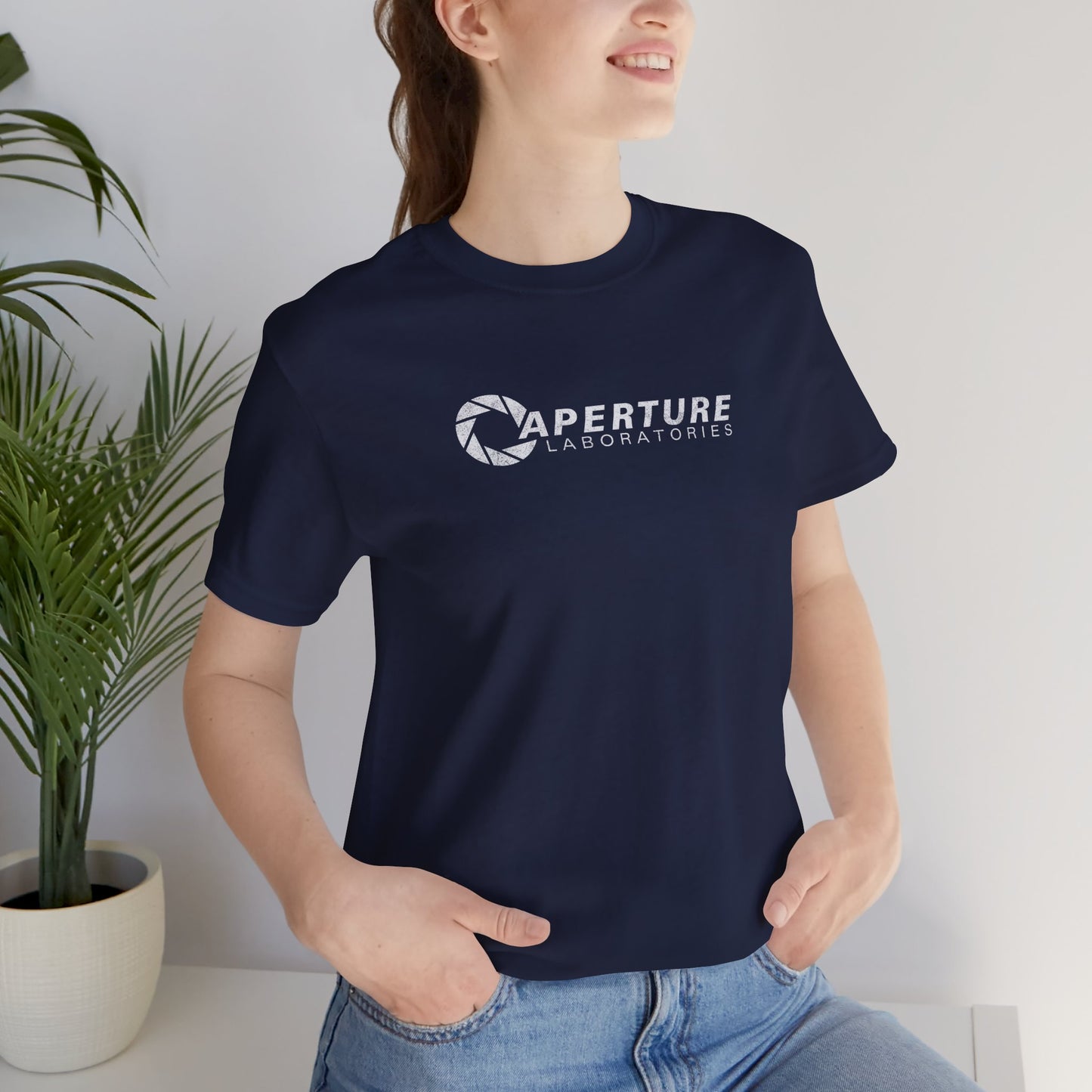 Woman model wearing a navy blue colored soft Bella+Canvas t-shirt with the Aperture Laboratories logo from the video game Portal and Portal 2 in a vintage ink-stamped distressed style. 