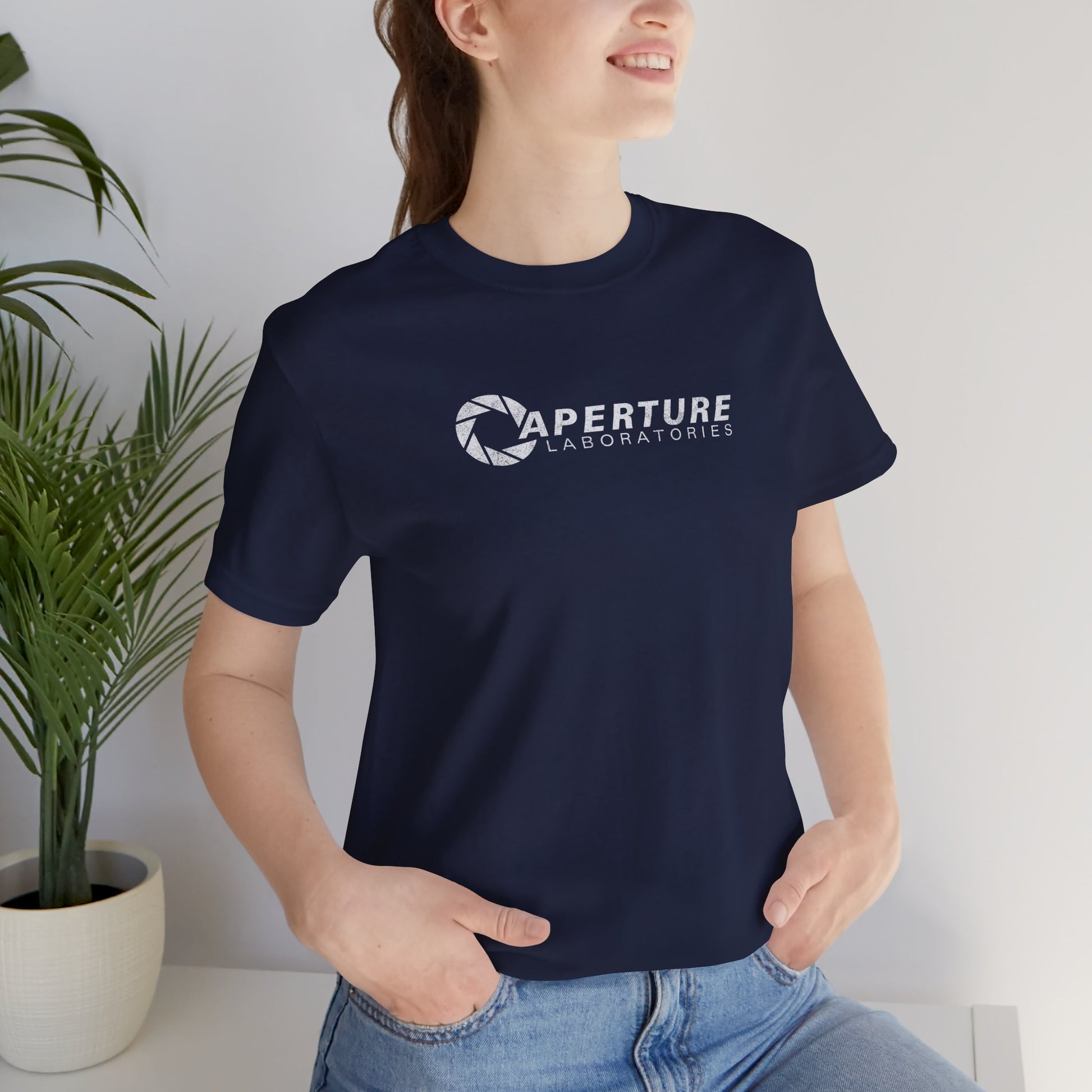 Woman model wearing a navy blue colored soft Bella+Canvas t-shirt with the Aperture Laboratories logo from the video game Portal and Portal 2 in a vintage ink-stamped distressed style. 