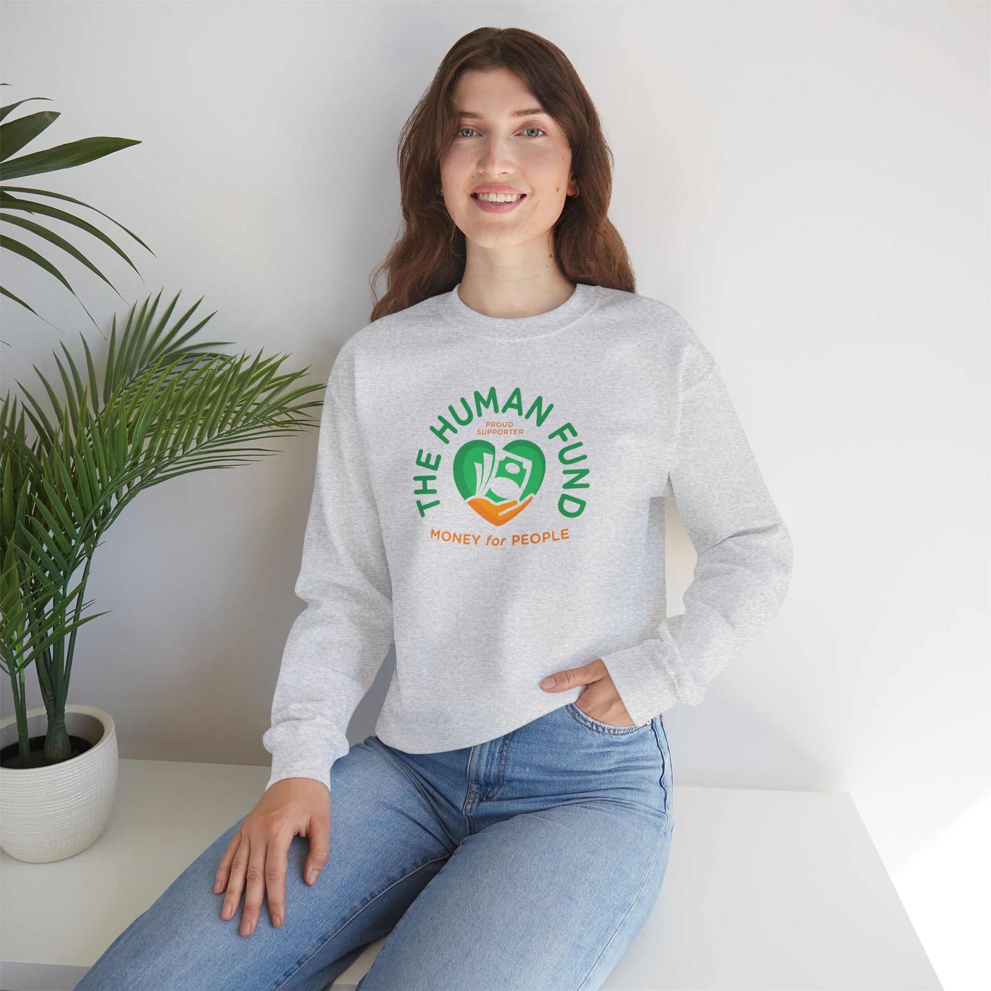 Person wearing a ash sweatshirt with 'The Human Fund' logo, sitting in a room with a plant.